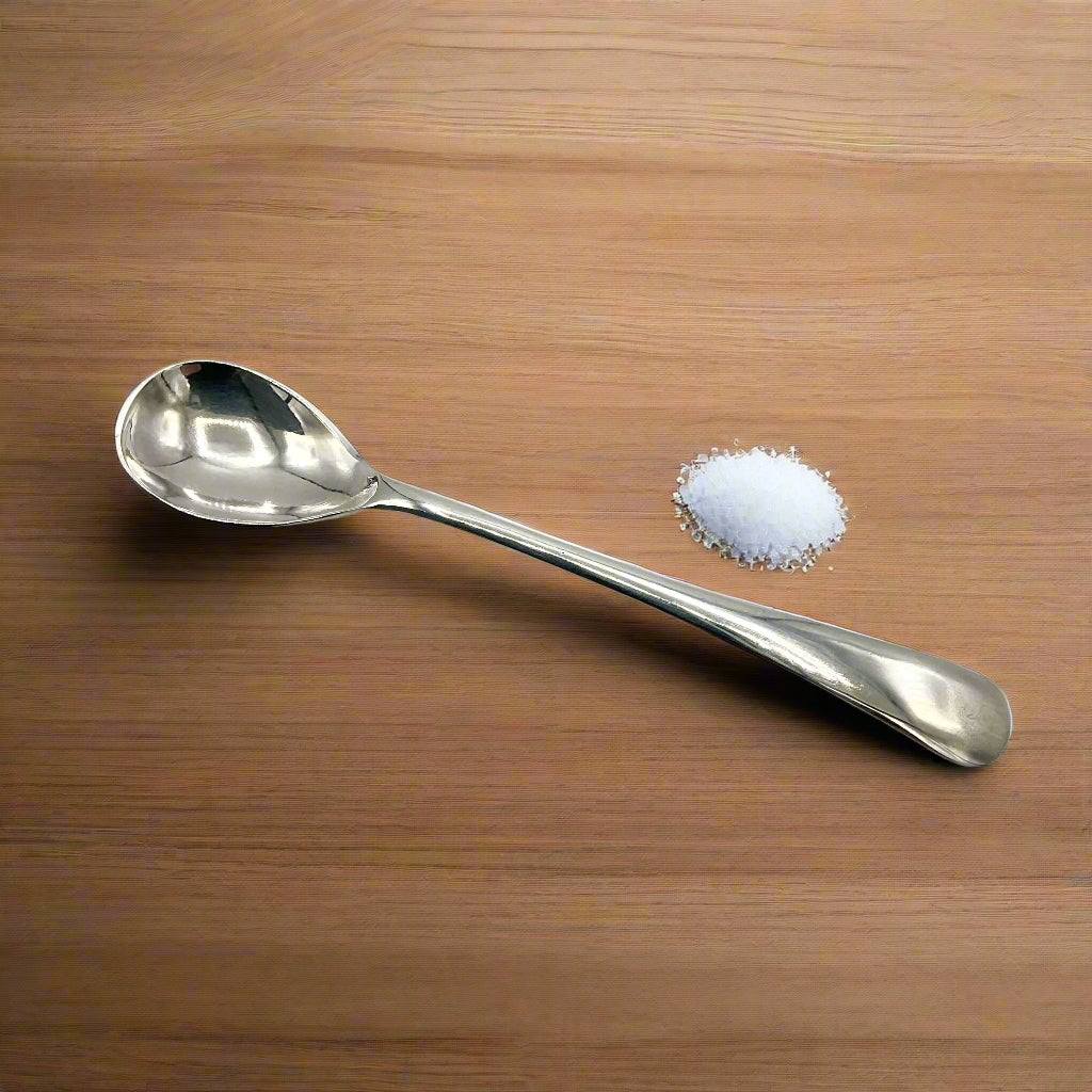 Silver salt spoon with a pile of salt next to it on a wooden table