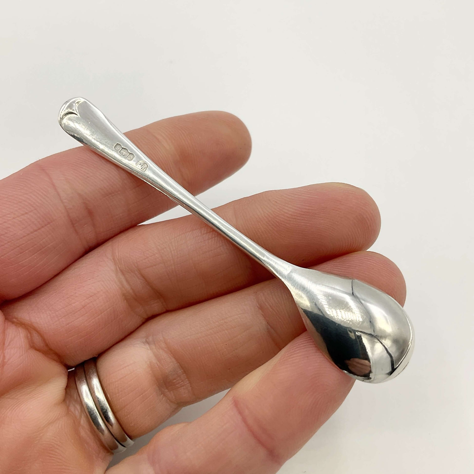 Silver salt spoon held in a hand with a hite background 