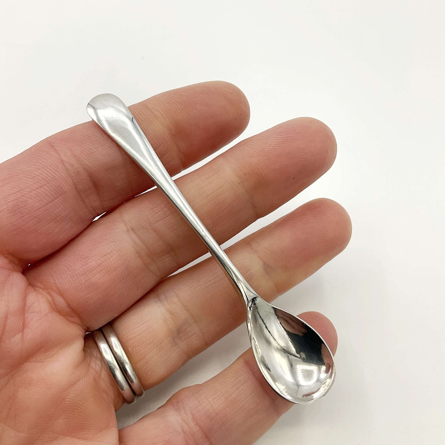 Silver salt spoon held in a hand with a white background 