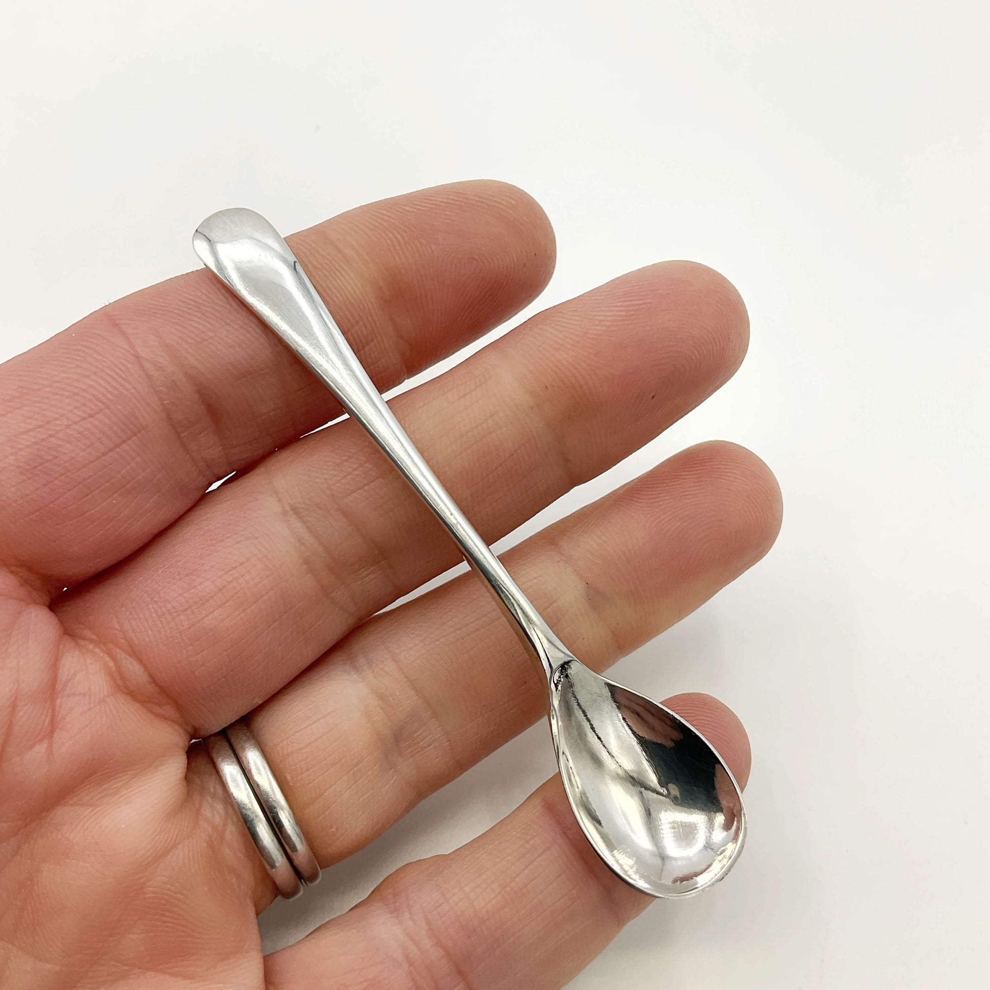 Silver salt spoon held in a hand with a white background 