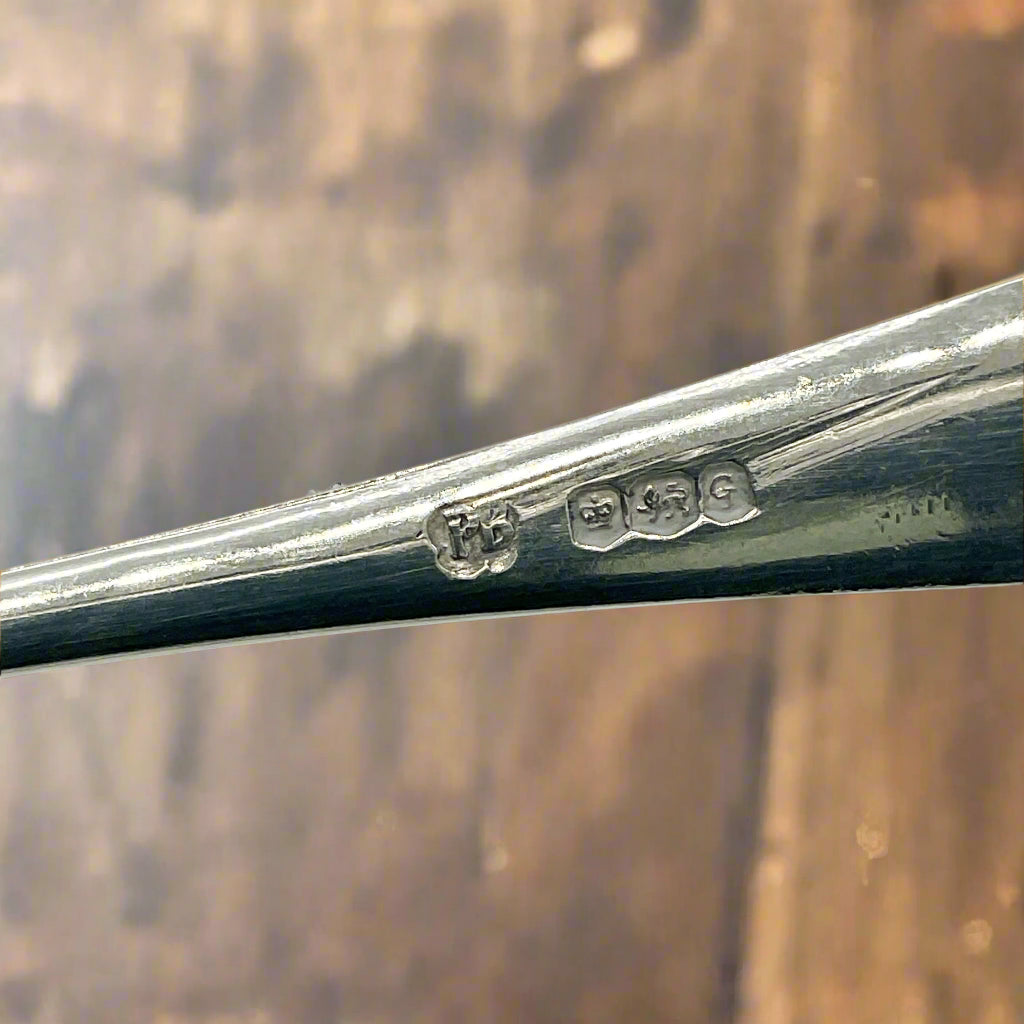 Hallmarks and maker’s mark on spoon handle with a wooden table in the background 