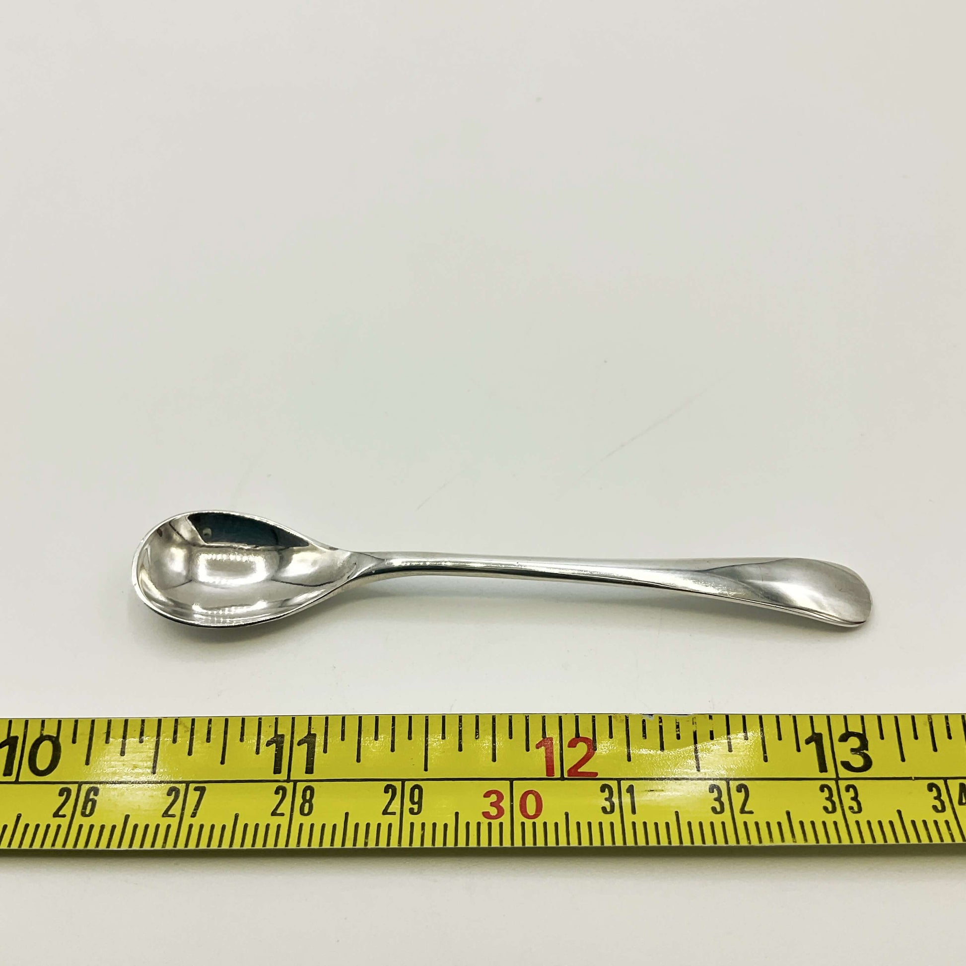 Silver salt spoon next to a tape measure showing the length as 7.7cm 