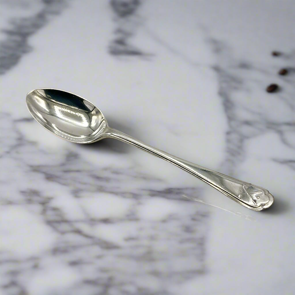Silver coffee spoon on a marble worktop with a couple of tiny cofee beans in the background 