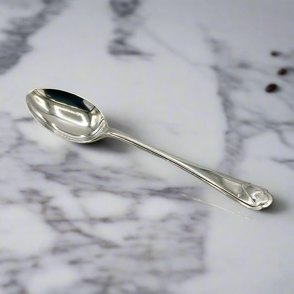 Silver coffee spoon on a marble worktop with a couple of tiny cofee beans in the background 