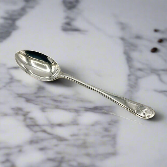 Silver coffee spoon on a marble worktop with a couple of tiny cofee beans in the background 