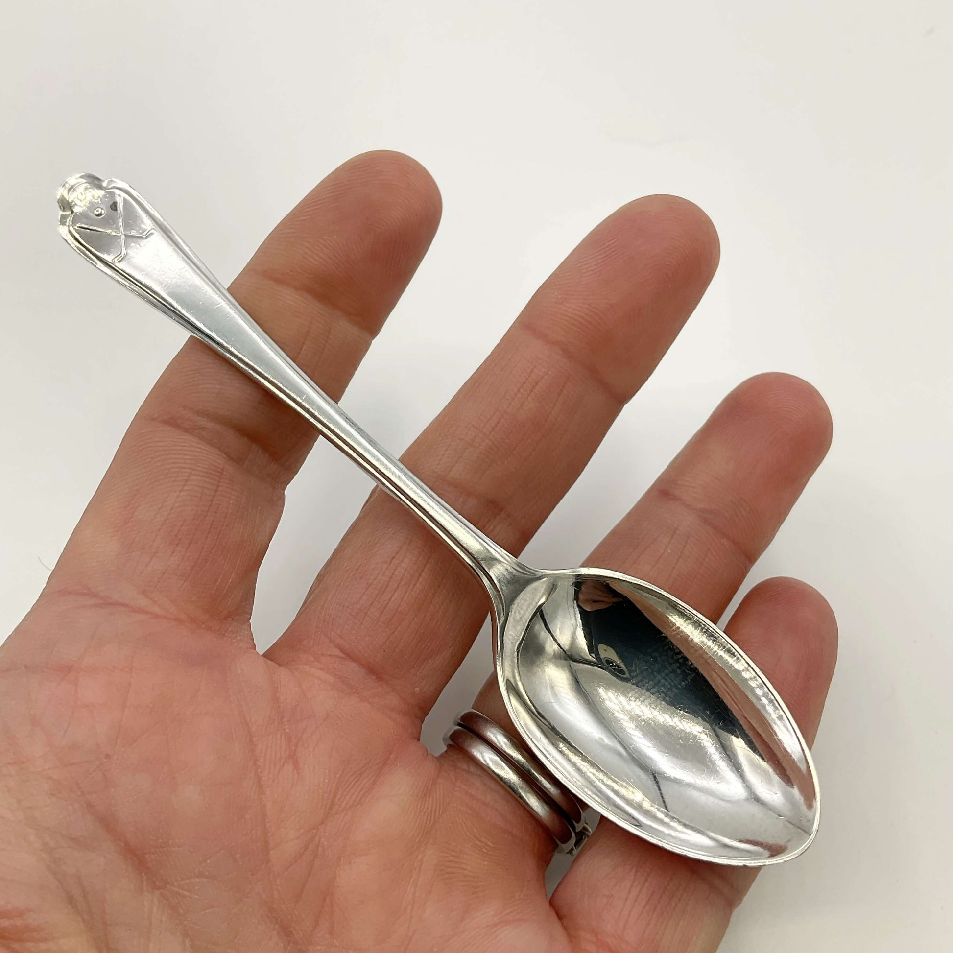 Silver coffee spoon held in a hand with a white background 
