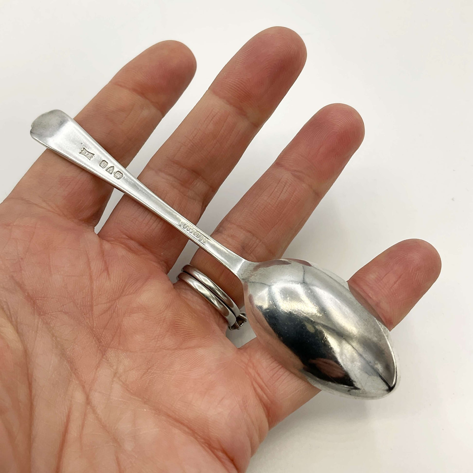 Back of silver coffee spoon held in a hand with a white background 
