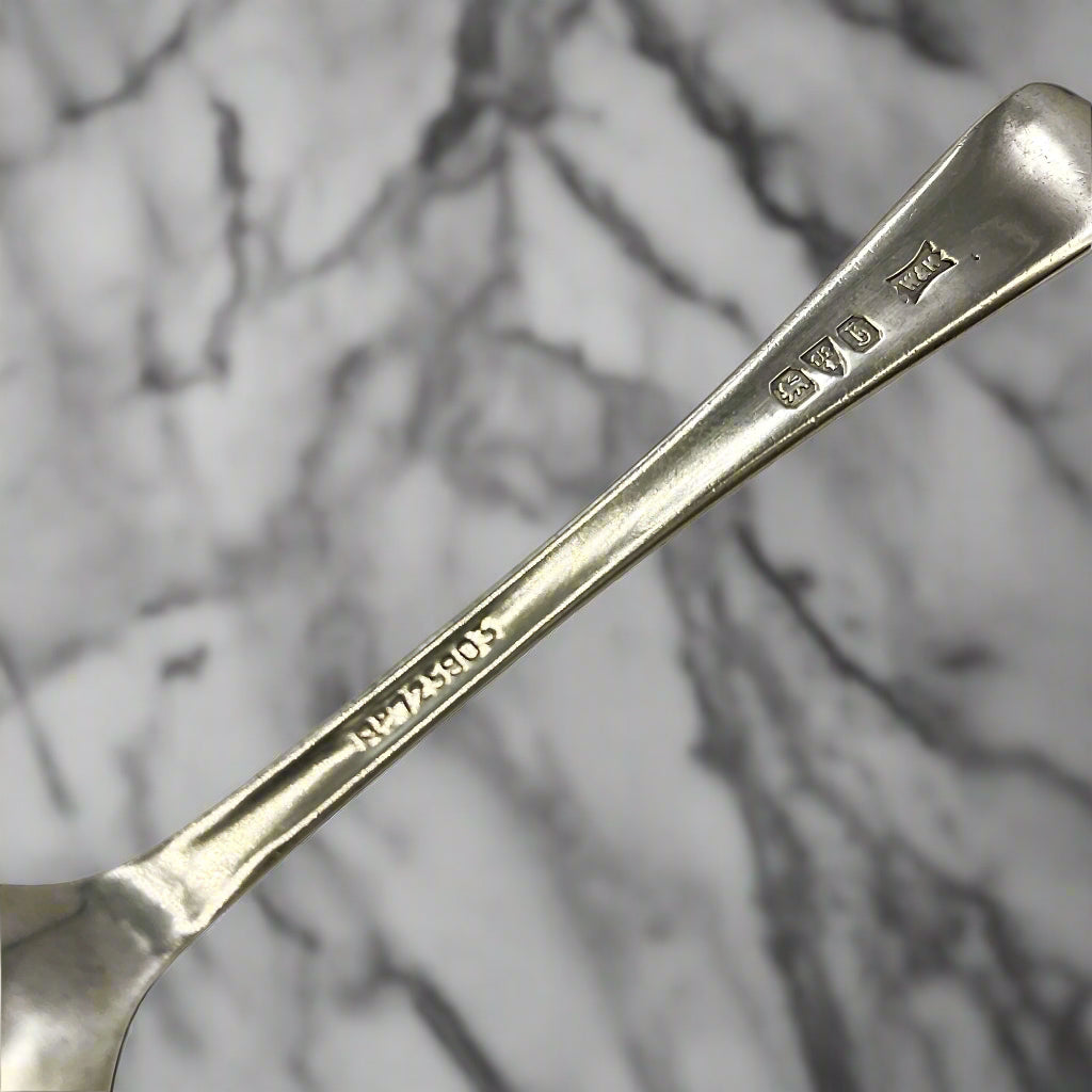 Back of silver spoon handle showing the hallmarks, maker’s mark and registered number 725803 with a marble background 