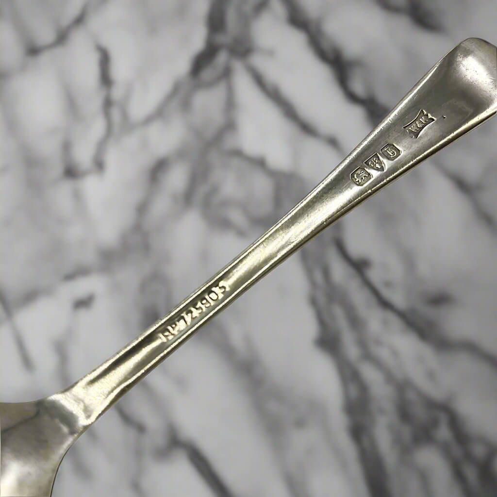 Back of silver spoon handle showing the hallmarks, maker’s mark and registered number 725803 with a marble background 