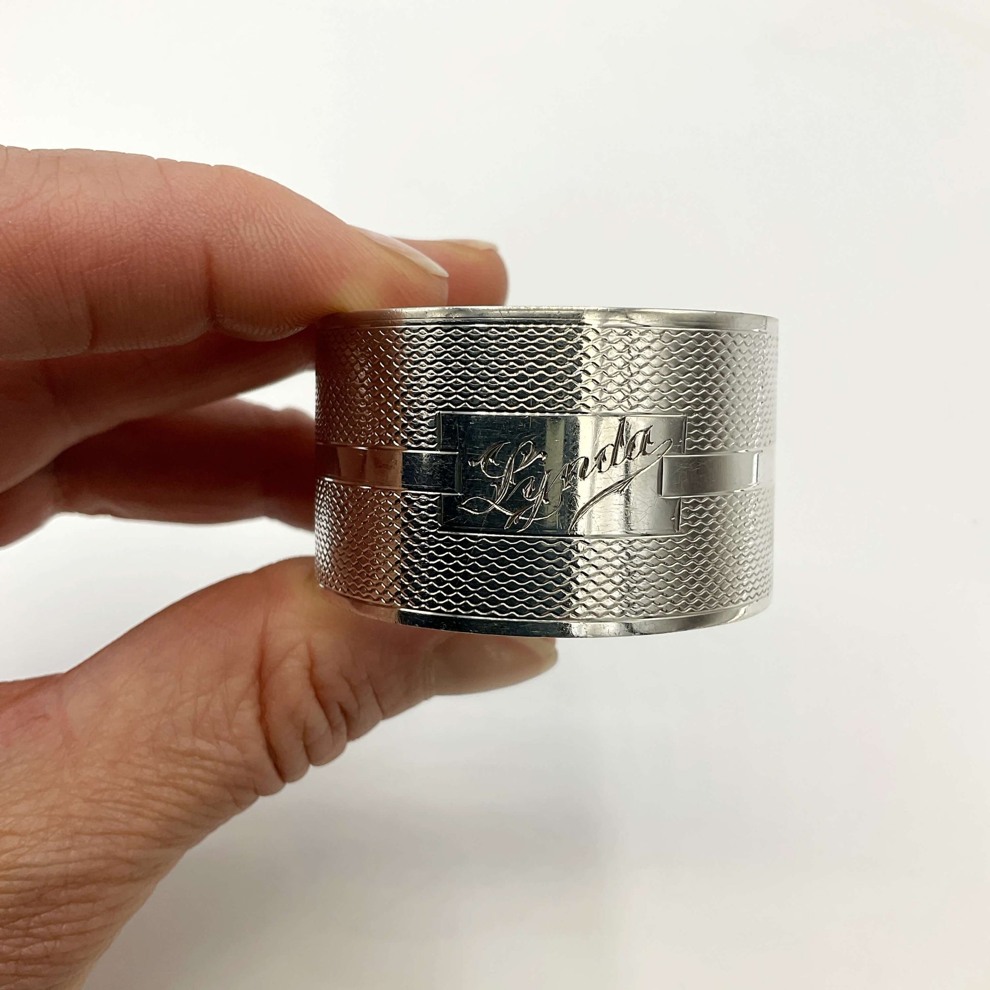 Silver napkin ring held in a hand with a white background 