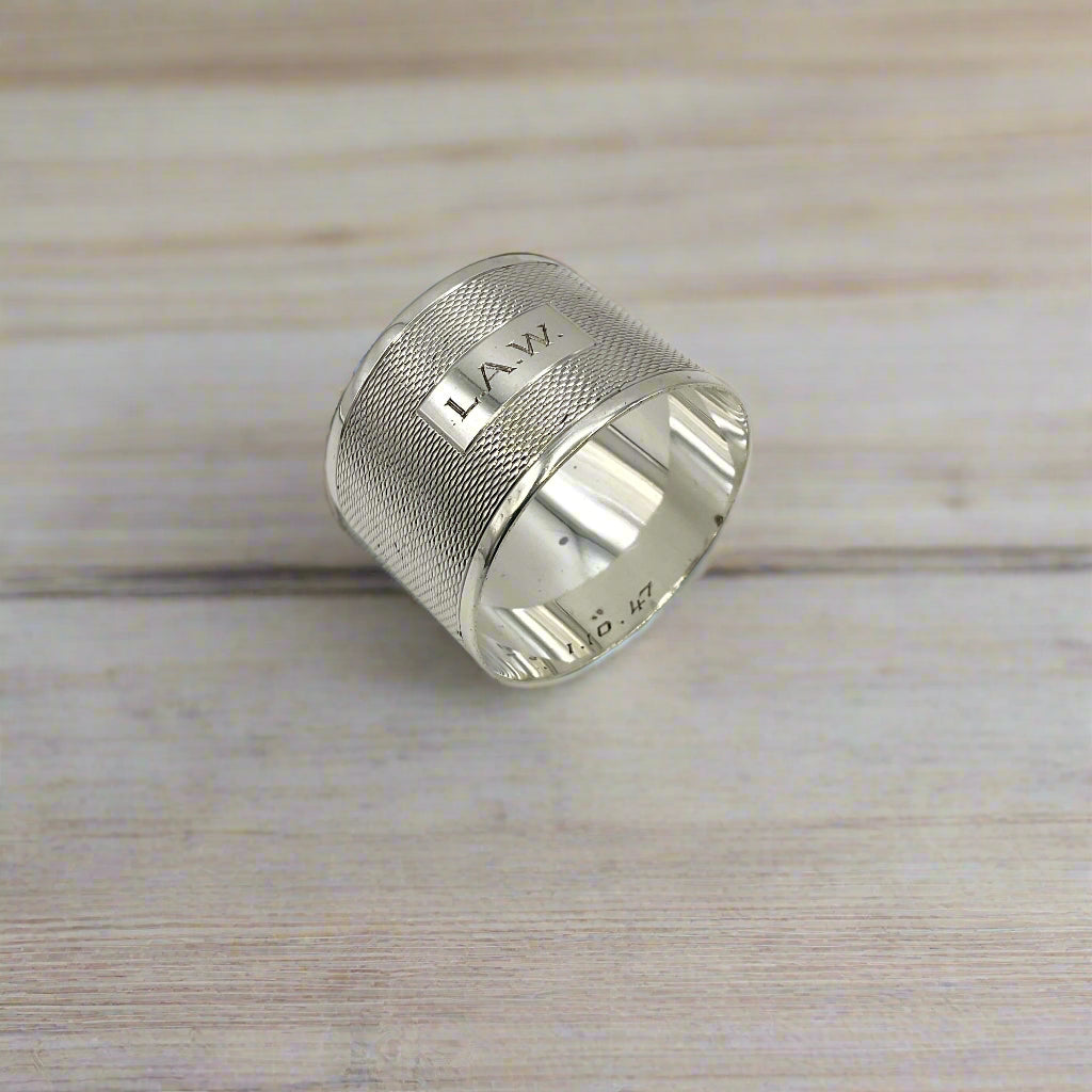 Silver napkin ring with LAW engraved on the front on a light wood table