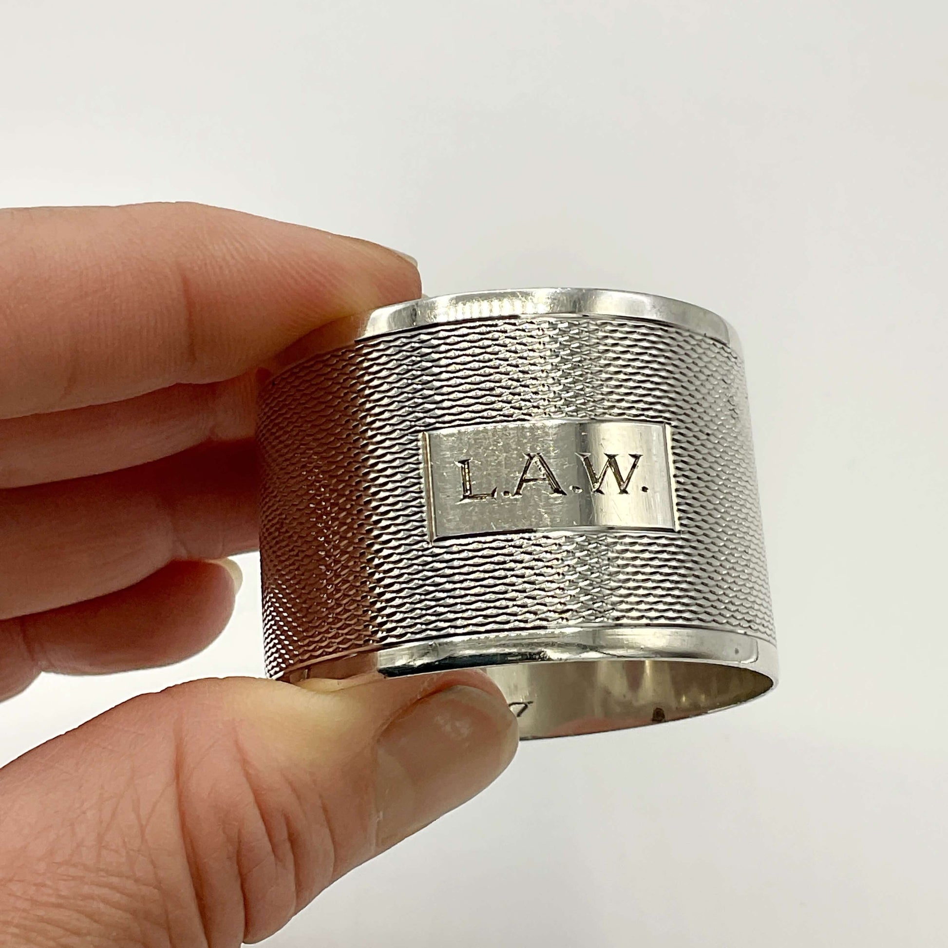 Silver napkin ring with LAW engraved on the front held between fingers with a white background 