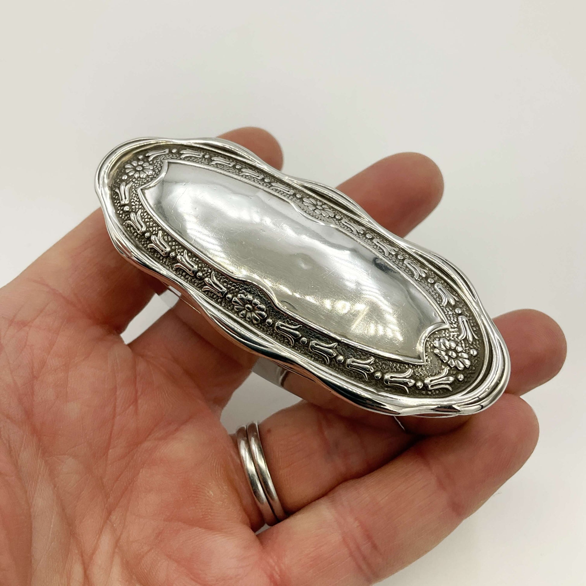 Small Antique silver jewellery box held in a hand on a white background 