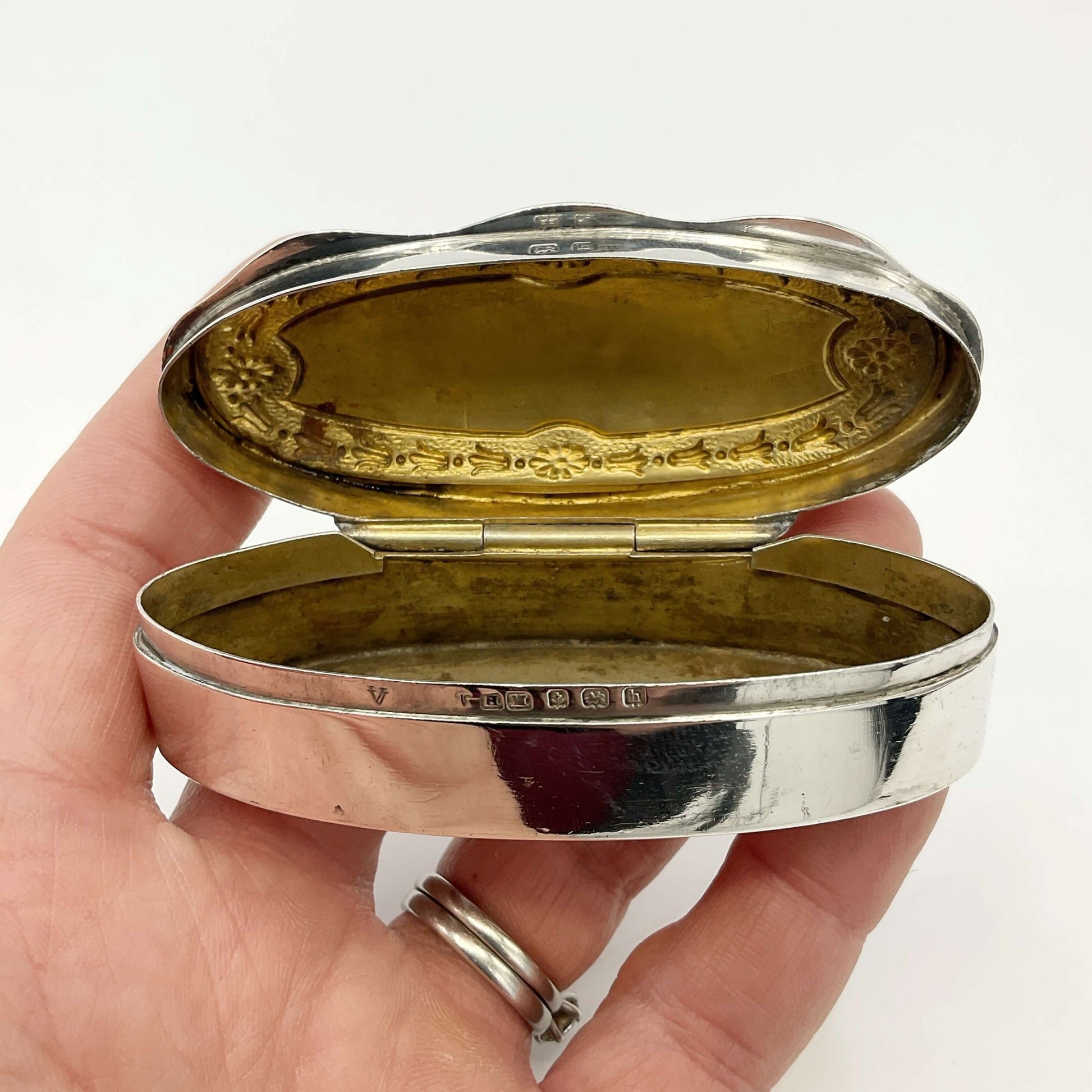 Small Antique silver jewellery box with the lid open showing a gilded interior held in a hand with a white background 