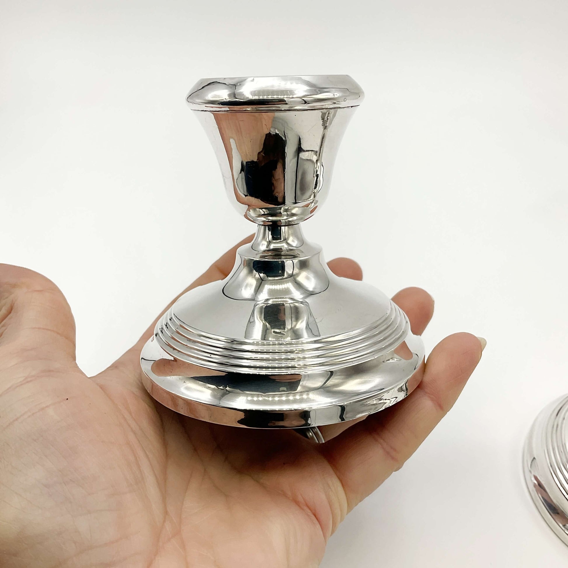 silver candle holder held in a hand with a second candle holder at the edge of the picture