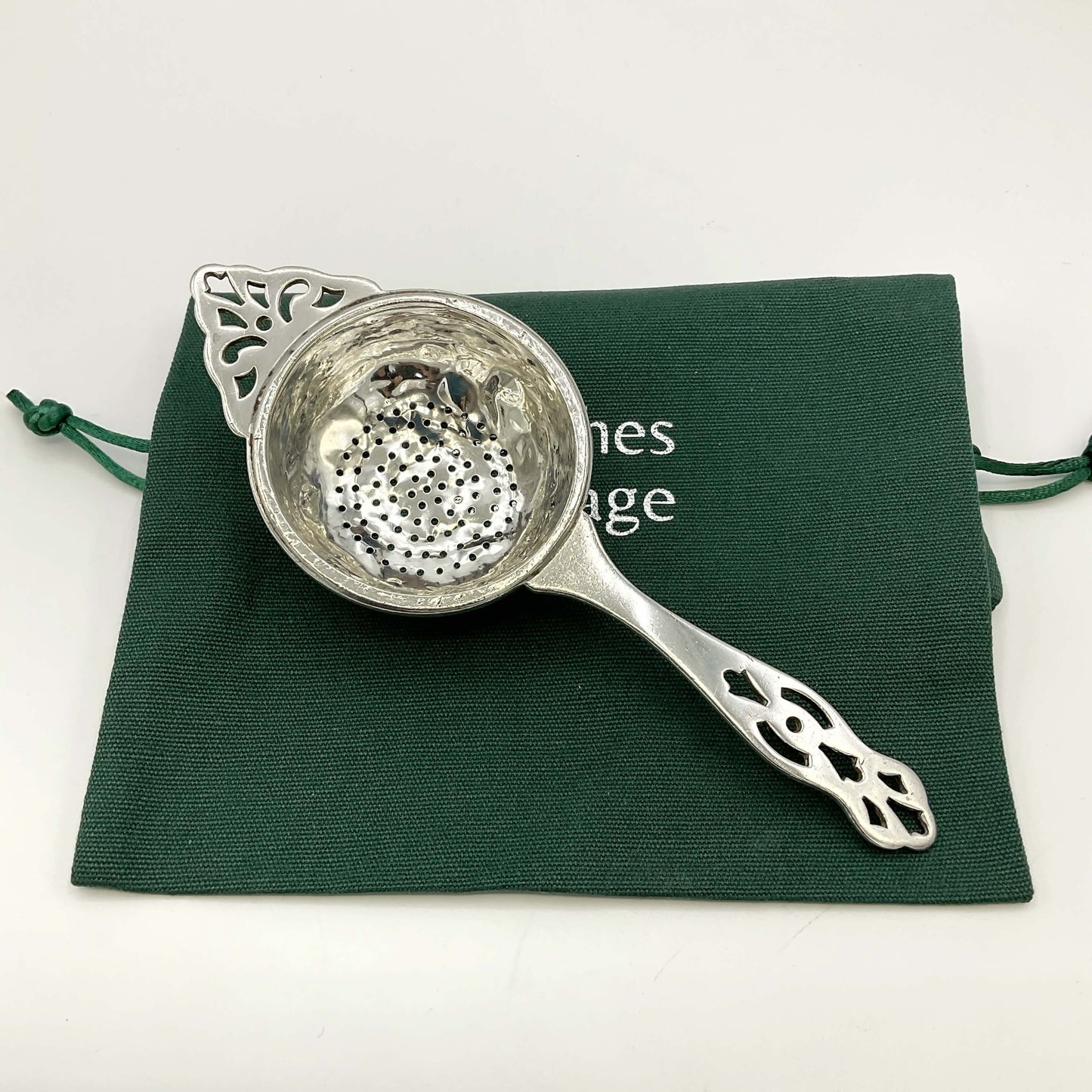 Silver tea strainer on a green gift bag and white background 