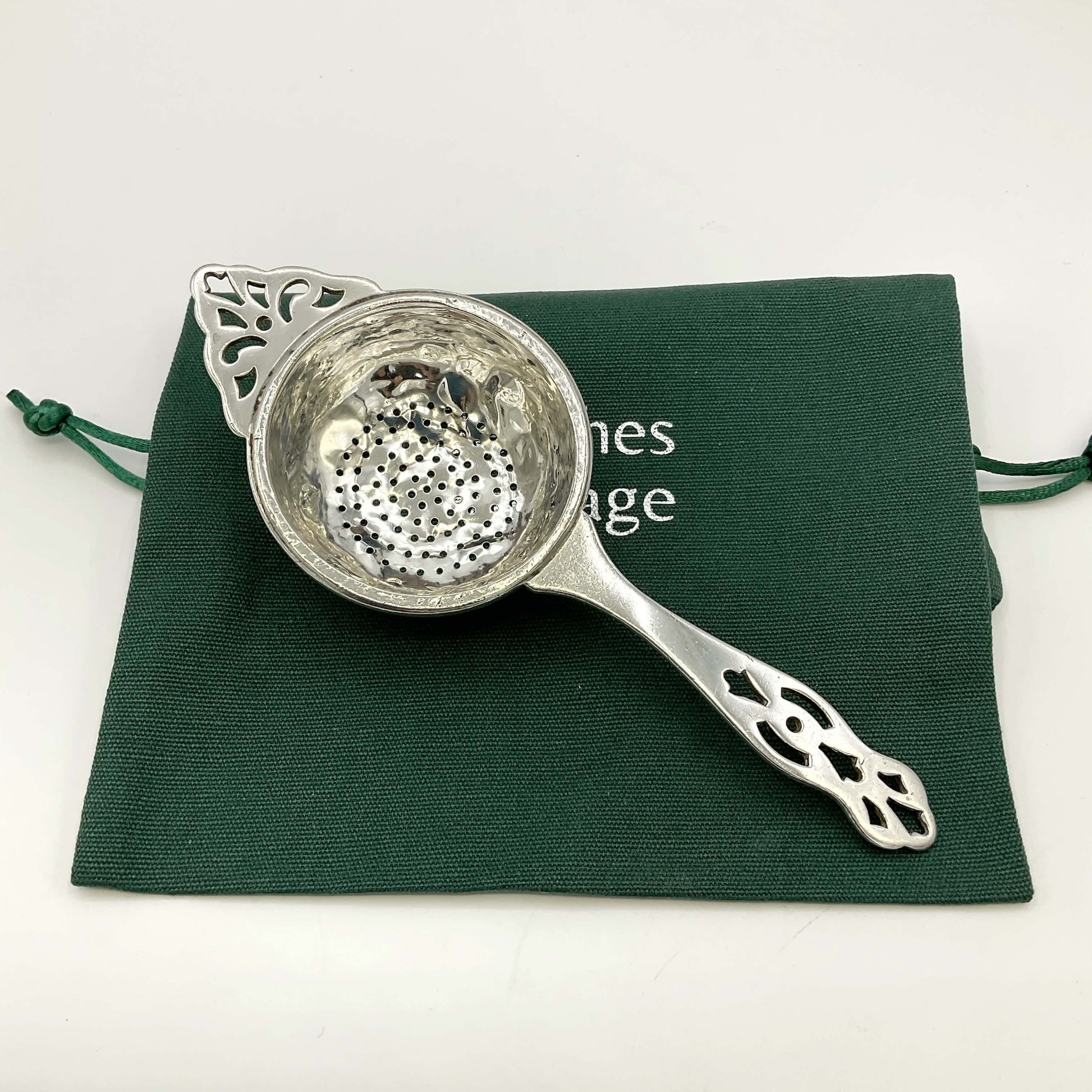 Silver tea strainer on a green gift bag and white background 
