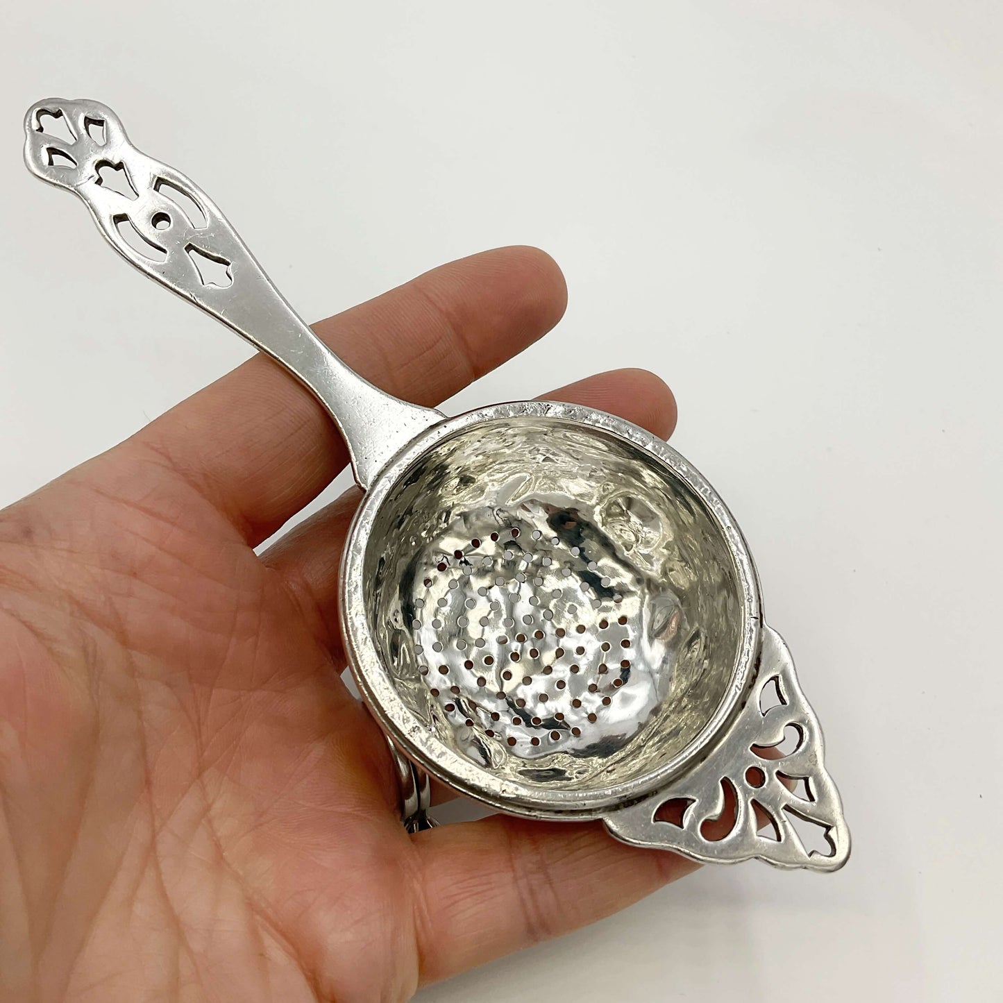 Silver tea strainer held in a hand with a white background 