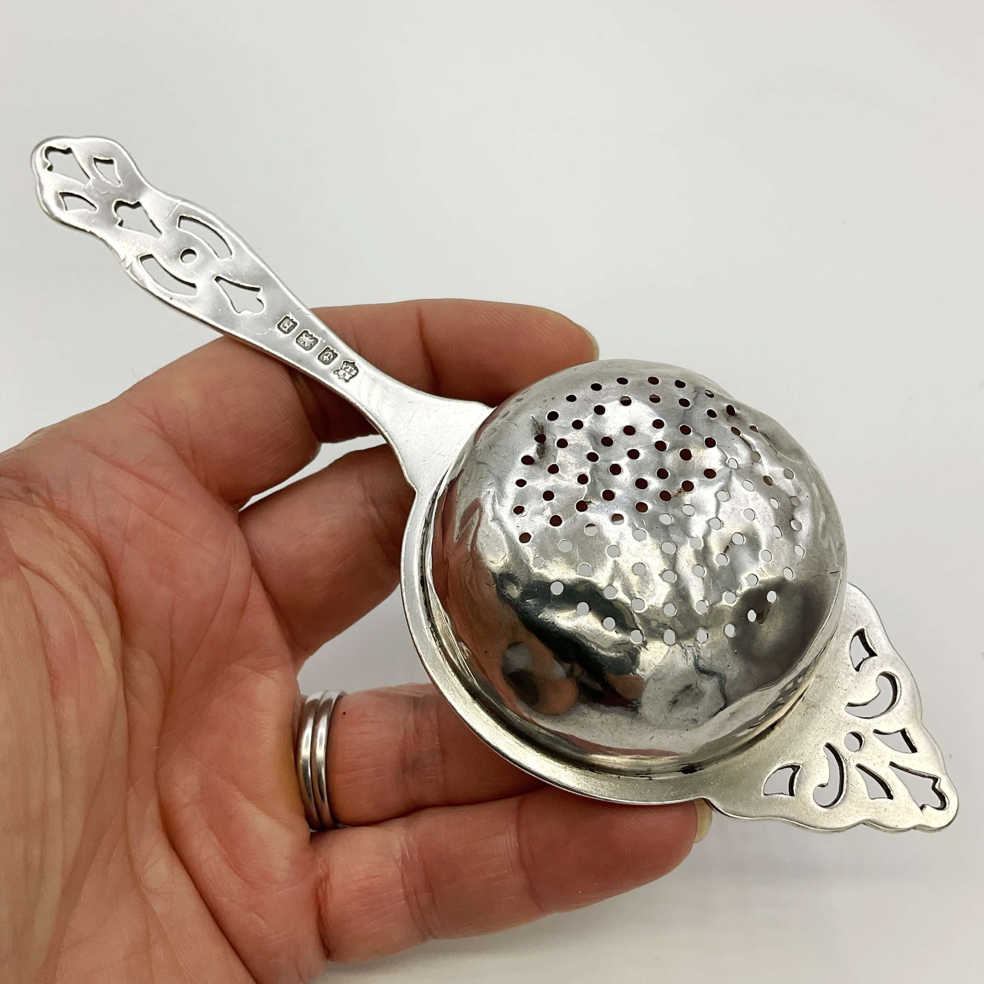 Back of silver tea strainer held in a hand with a white background 