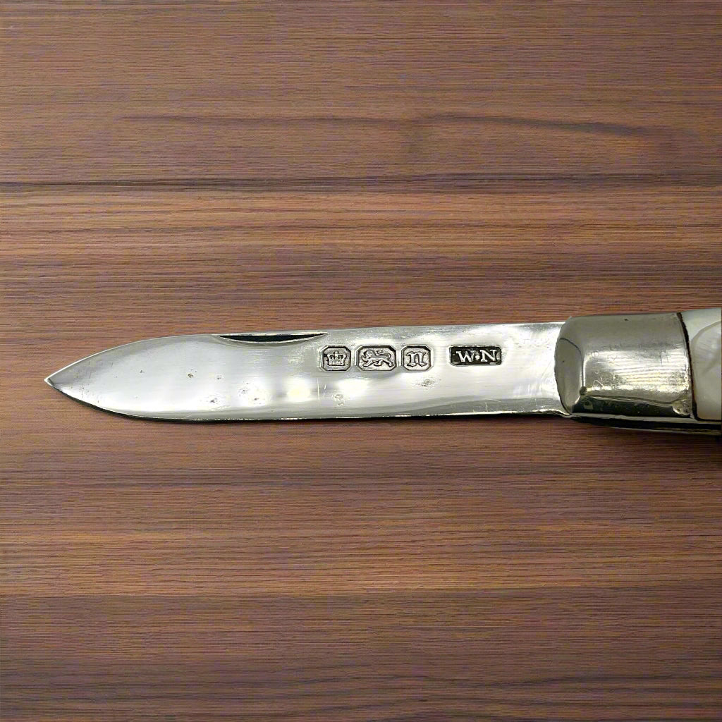 Hallmarks on a silver fruit knife blade on a dark wood table