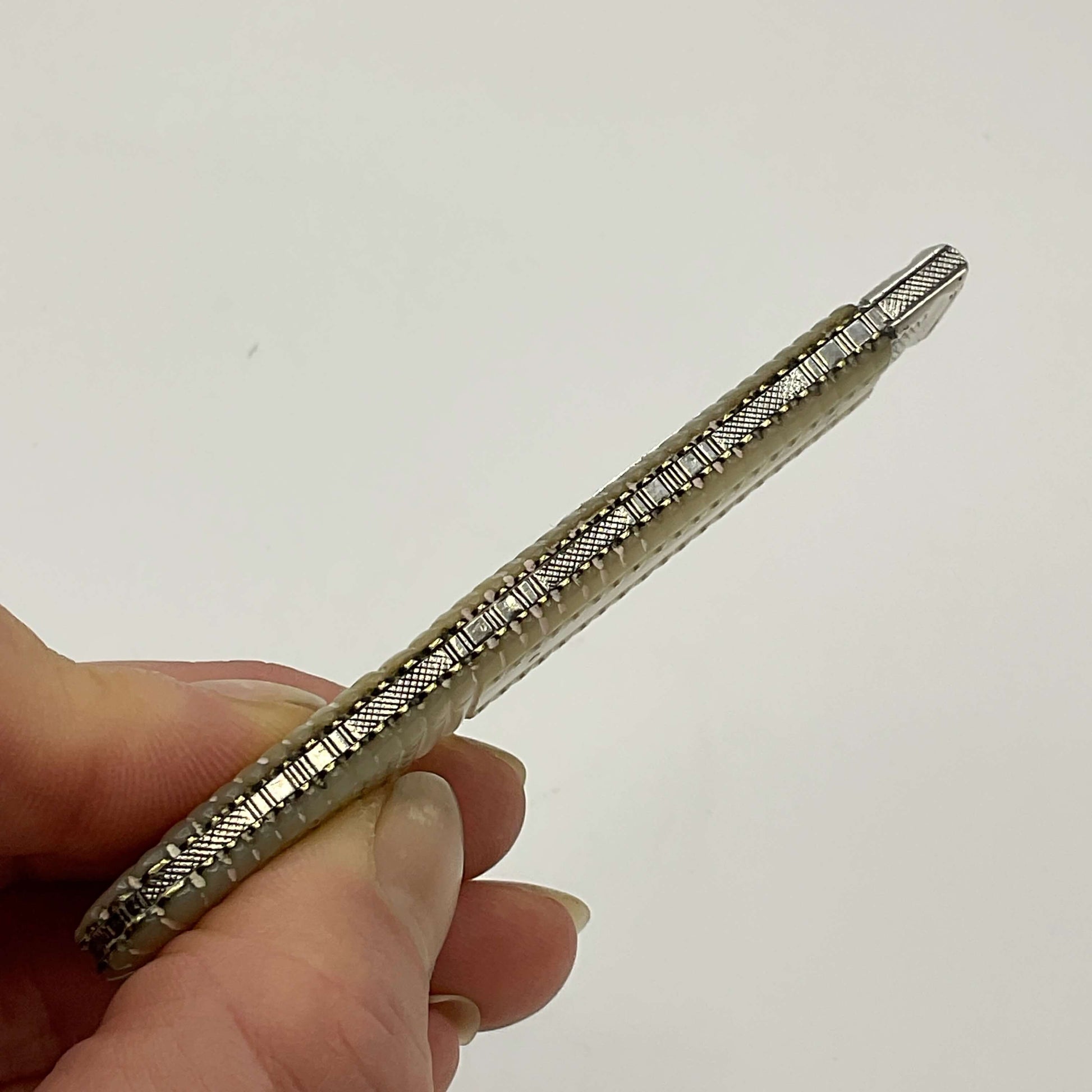 Antique silver fruit knife With a patterned back held in a hand.
