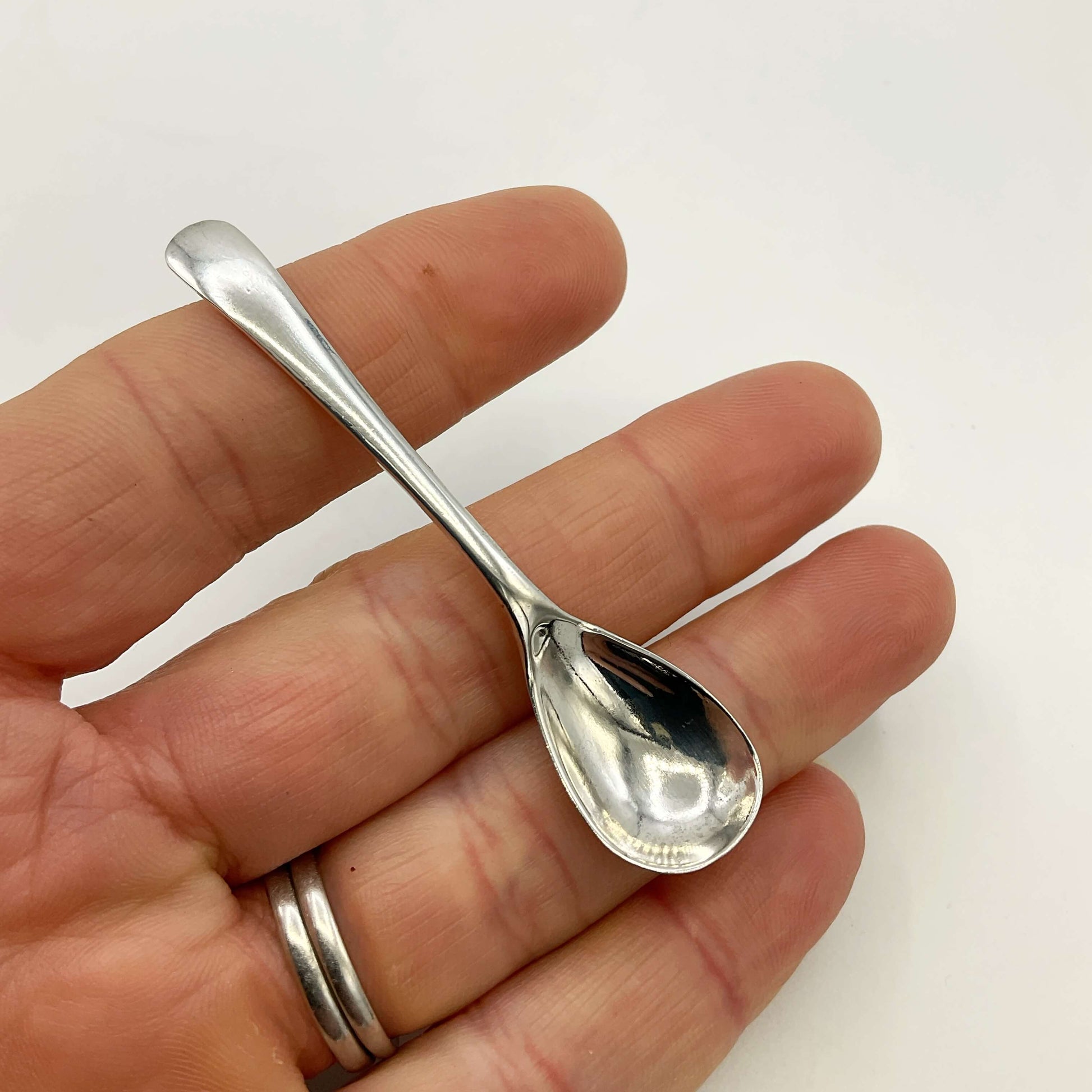 Small silver spoon held in a hand against a white background