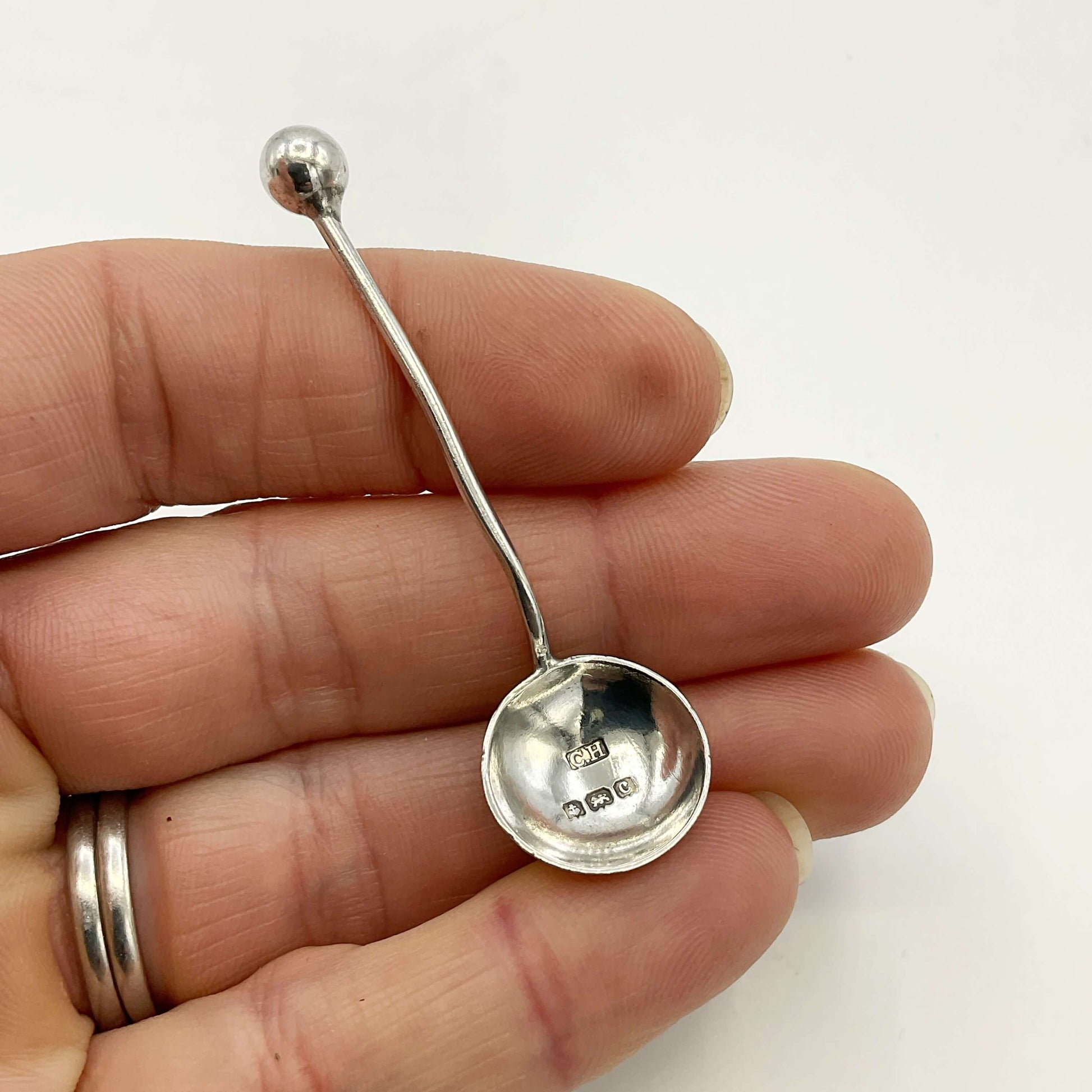 antique silver salt spoon held in a hand with a white background