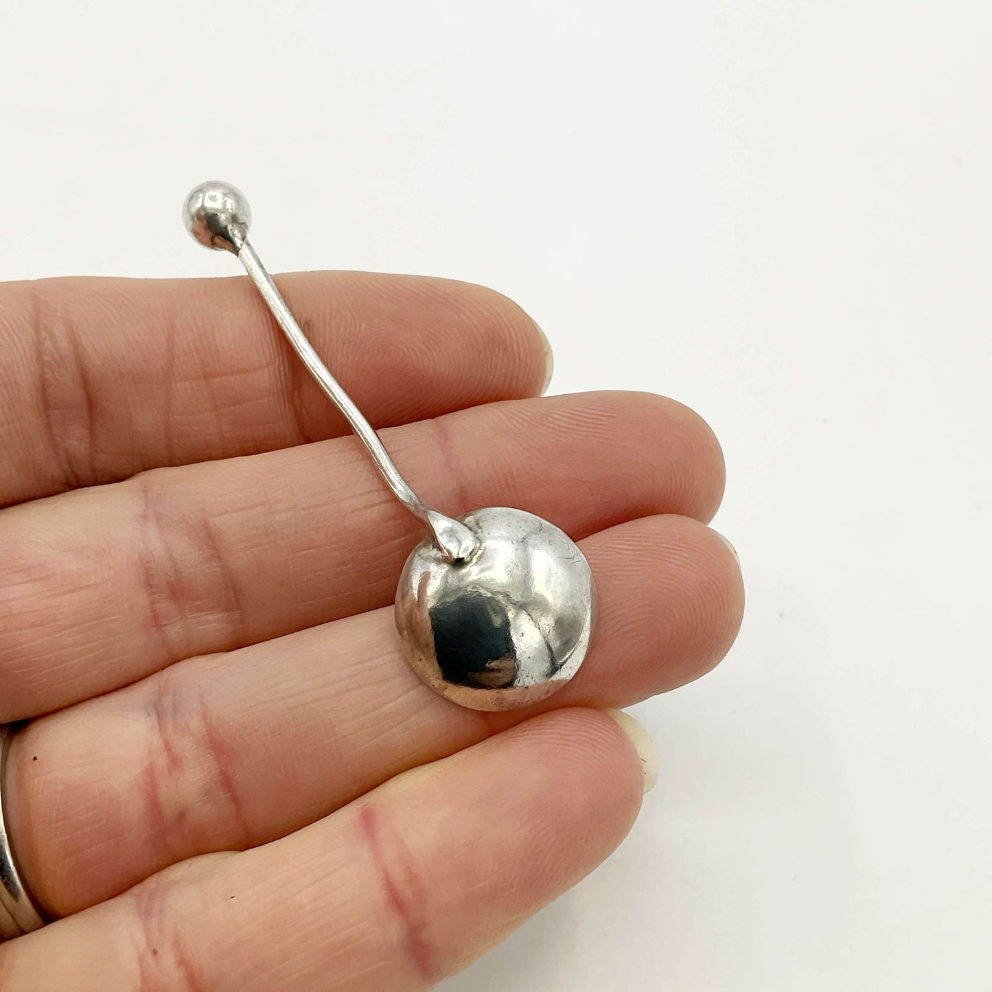 back of a Silver spoon held on fingers on a white background