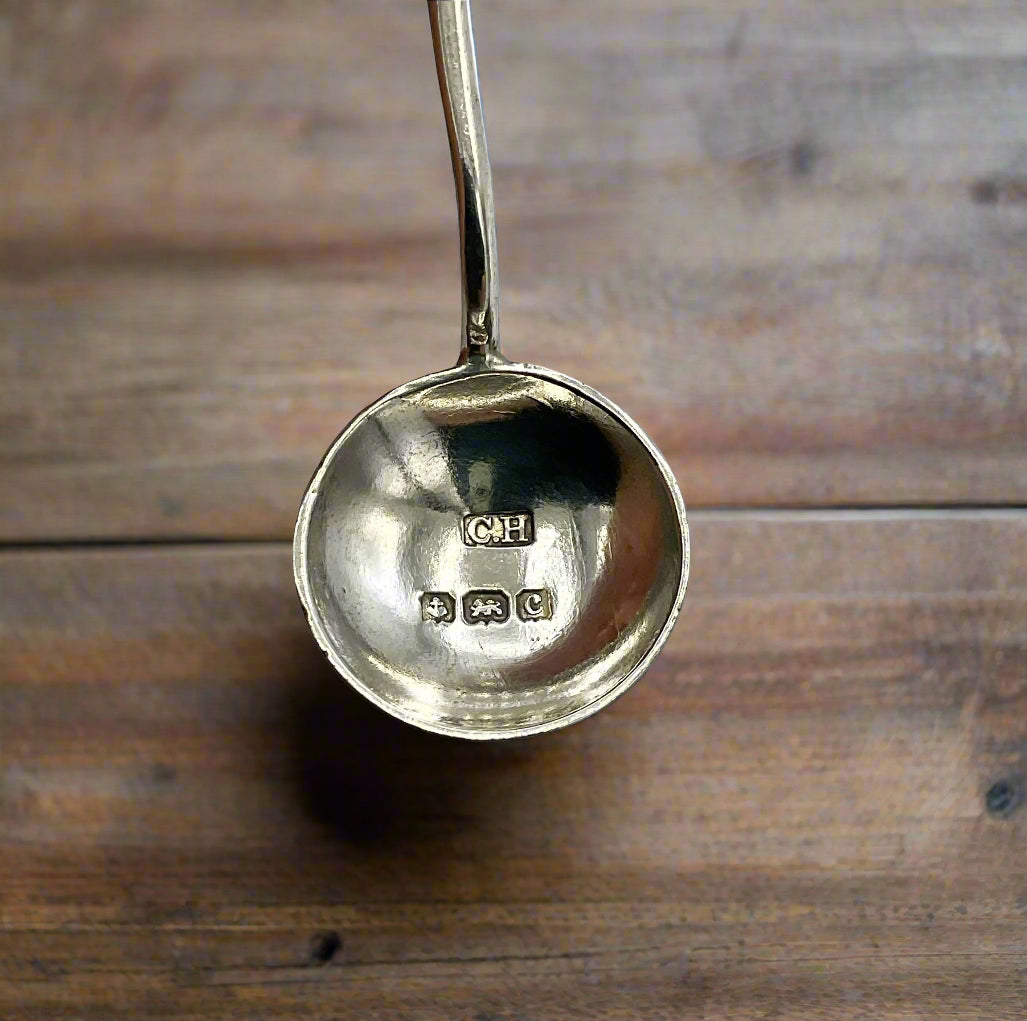 Silver spoon with visible hallmarks with a wood table in the background 