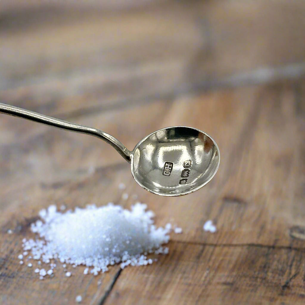 salt spoon with visible hallmarks above a wood table and a pile of salt