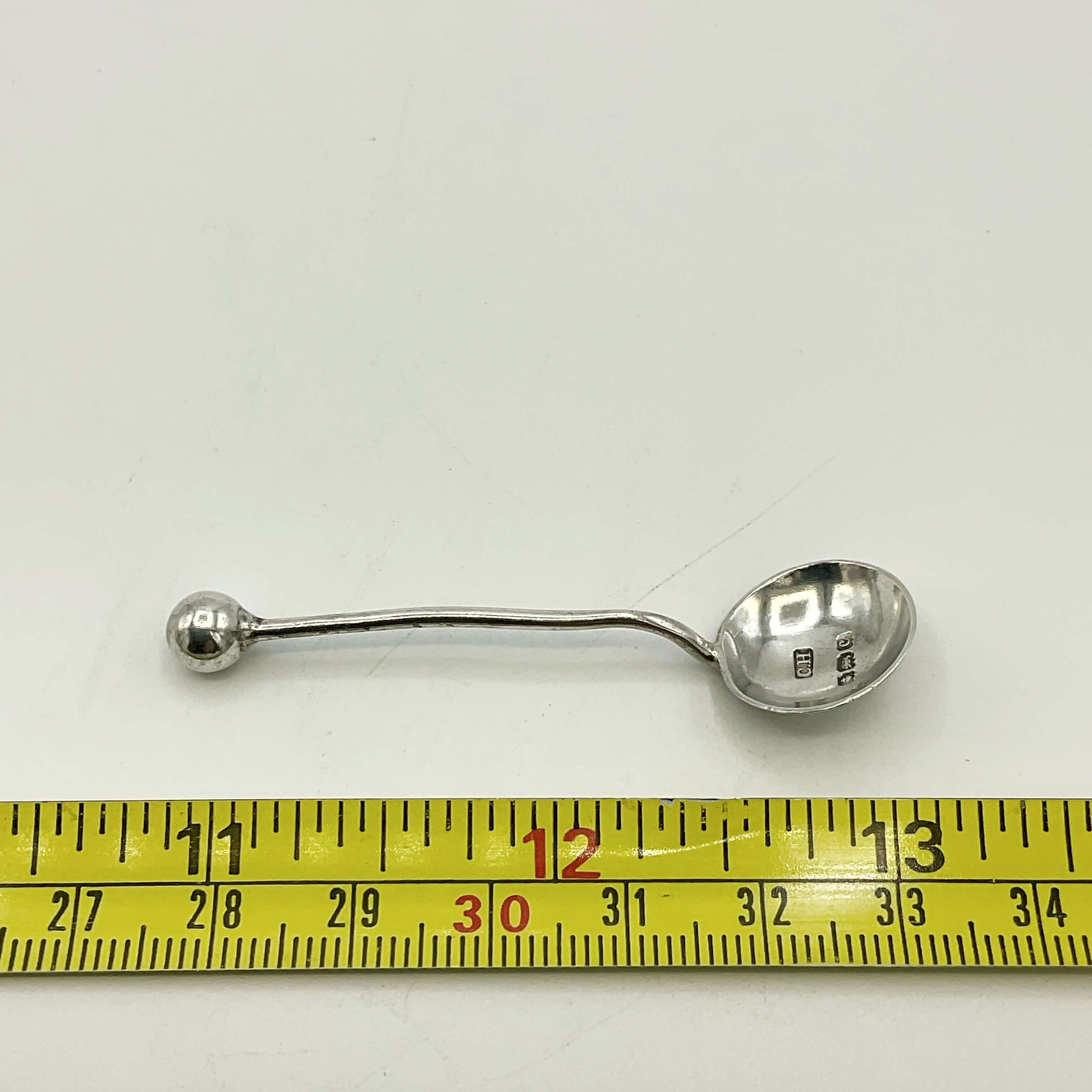 Silver spoon with measurement tape showing its length on a white background