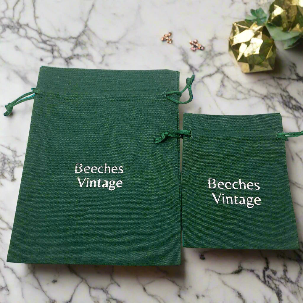 Two green drawstring bags with 'Beeches Vintage' text on a marble worktop