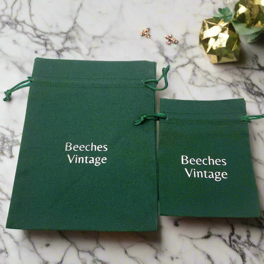Two green drawstring bags with 'Beeches Vintage' text on a marble worktop