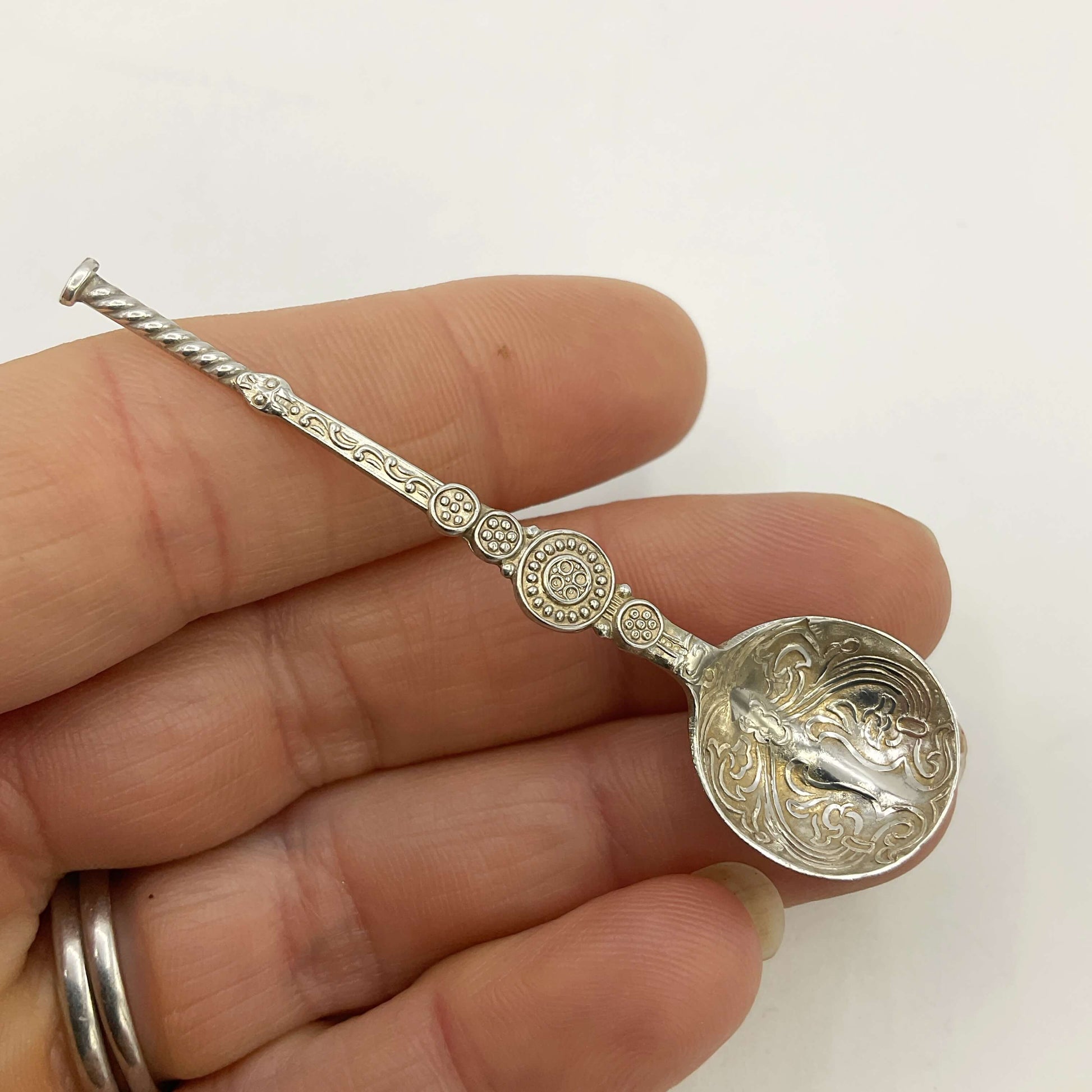 Decorative silver spoon held in a hand against a white background