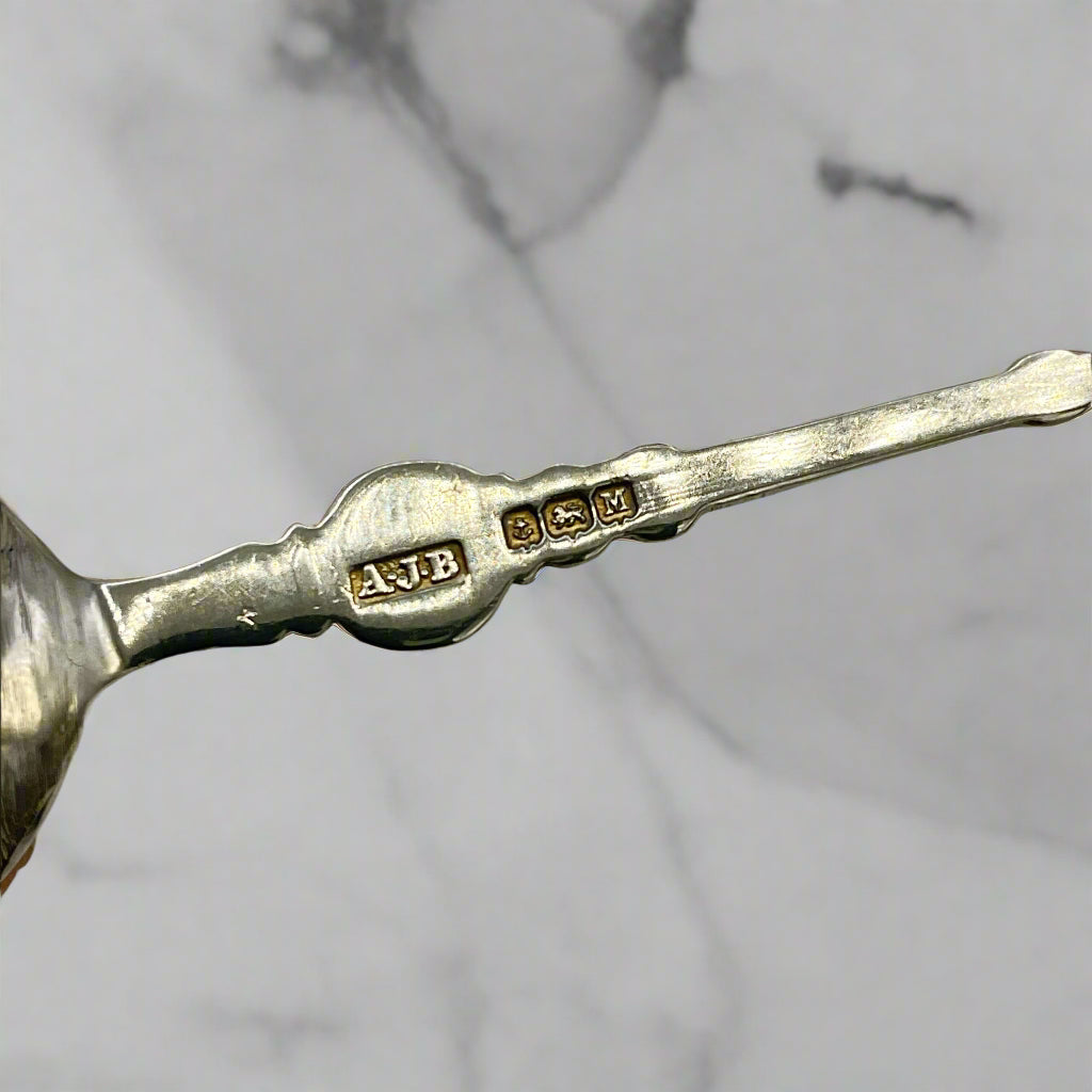 Close-up of a silver spoon with 'AJB' and hallmarks on a marble background