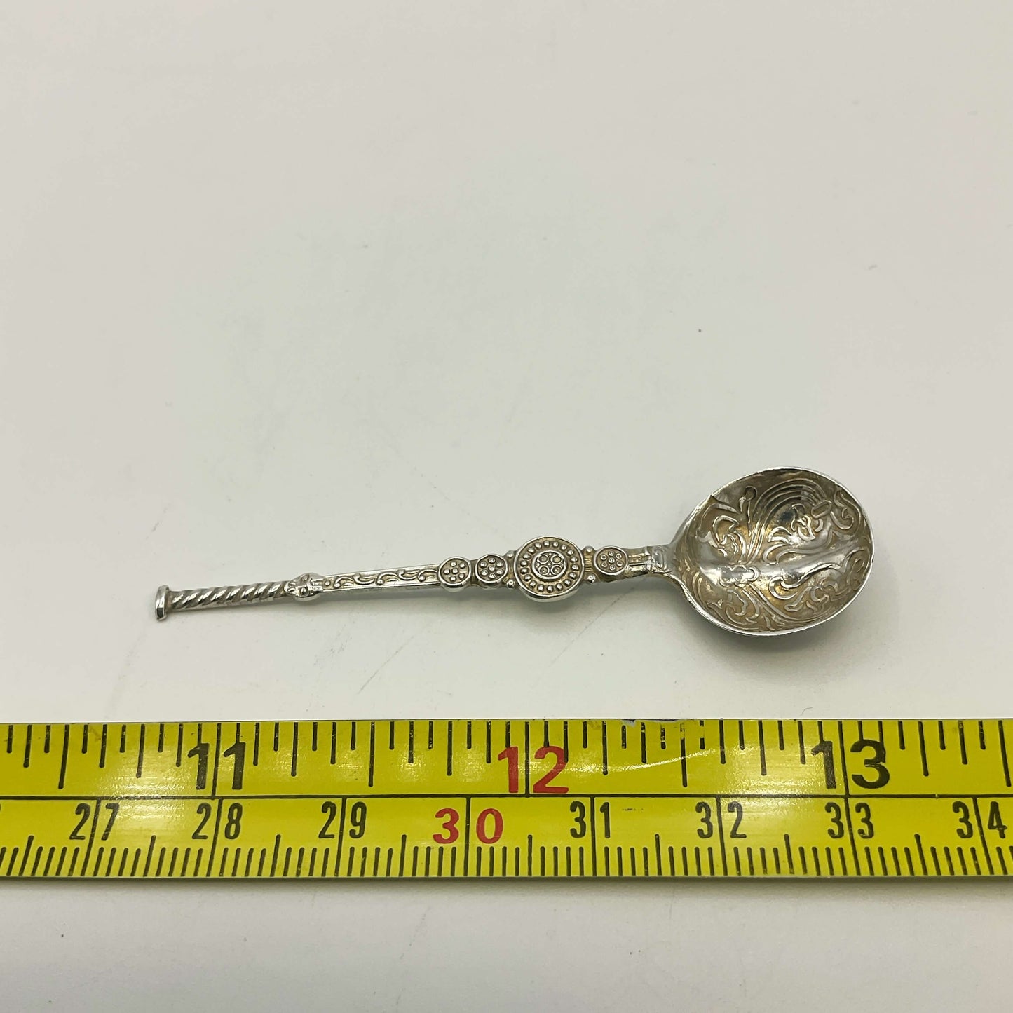 Silver decorative spoon next to a measuring tape on a white background