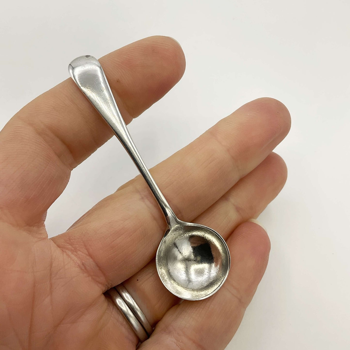 Small silver spoon held in a hand against a white background