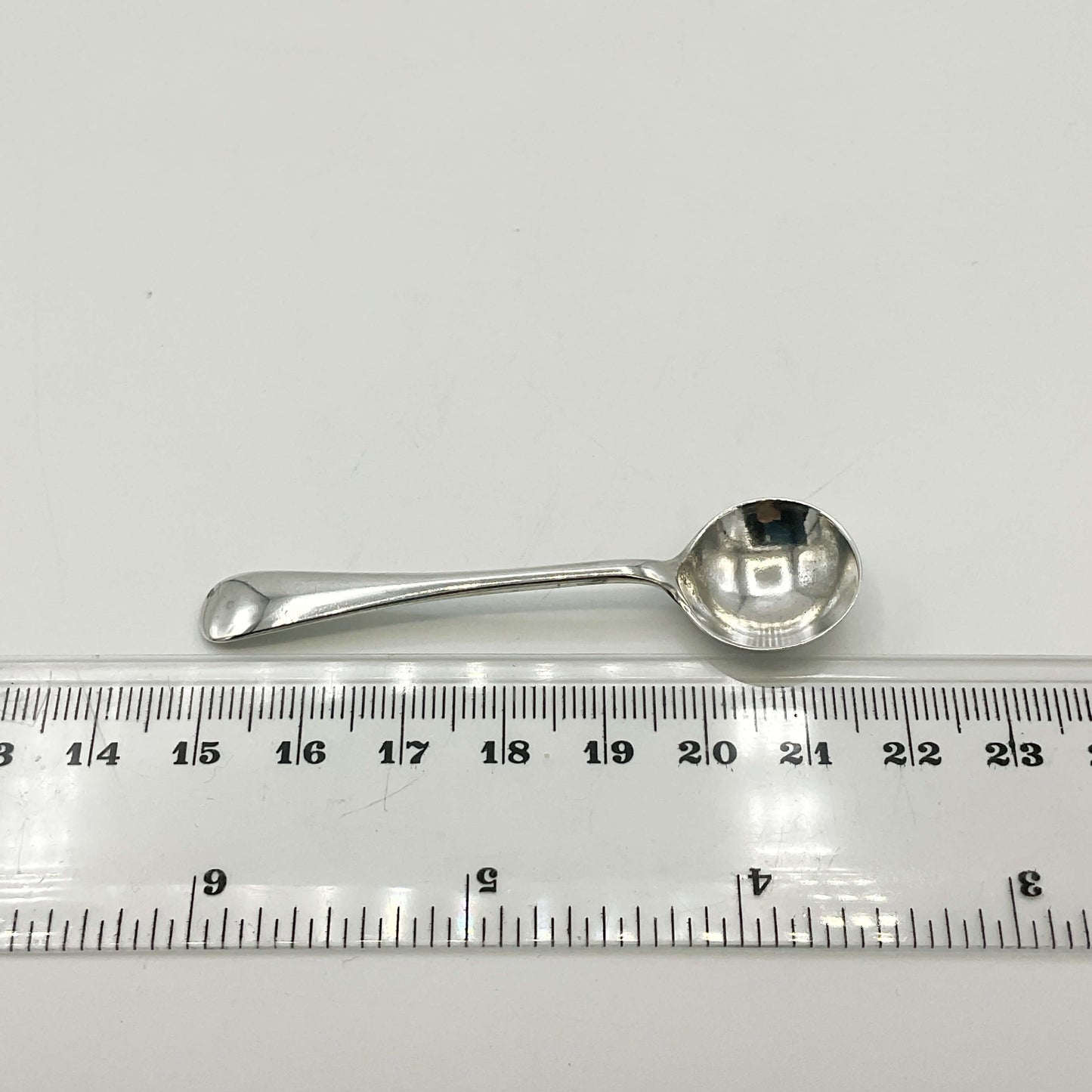 Silver spoon next to a ruler on a white background