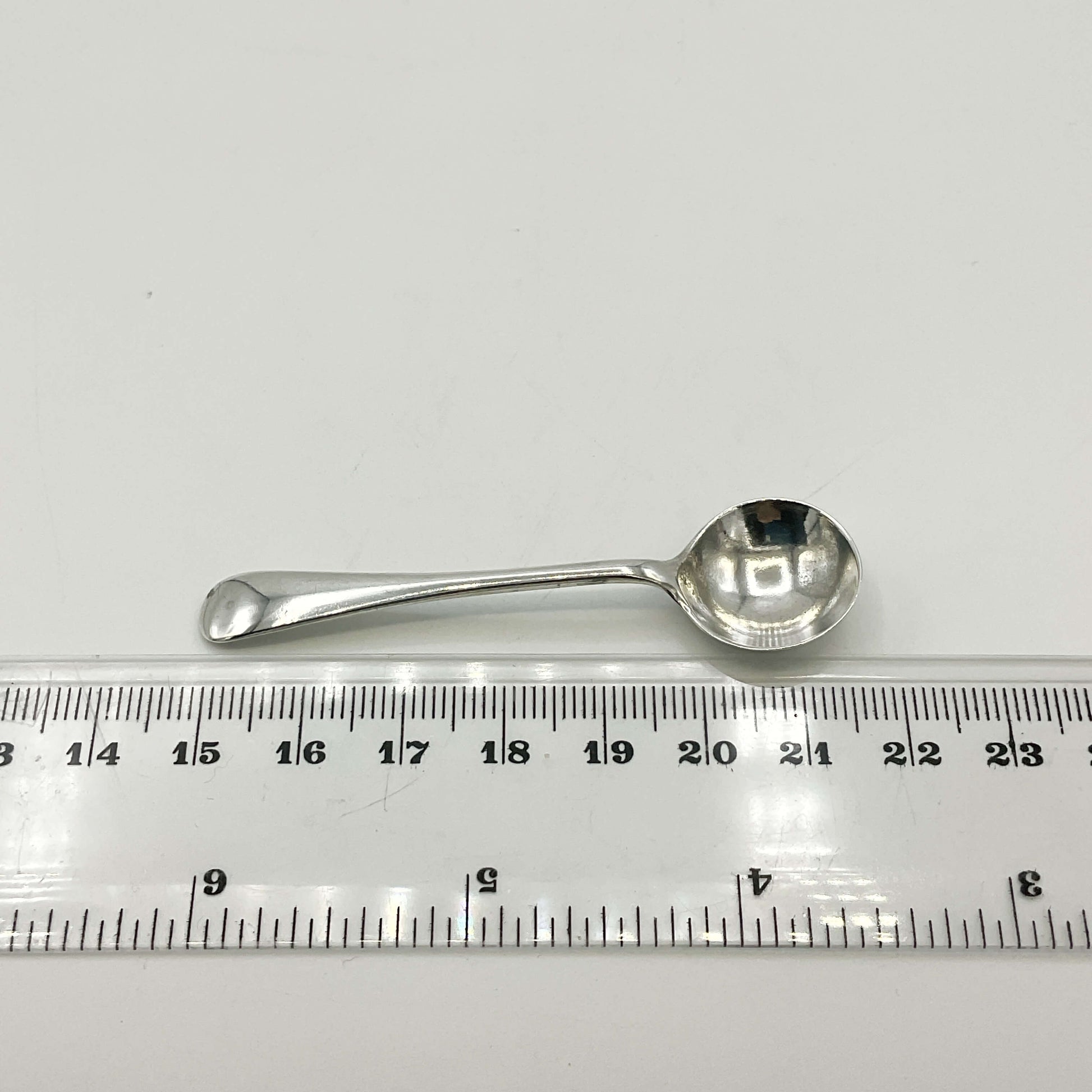 Silver spoon next to a ruler on a white background