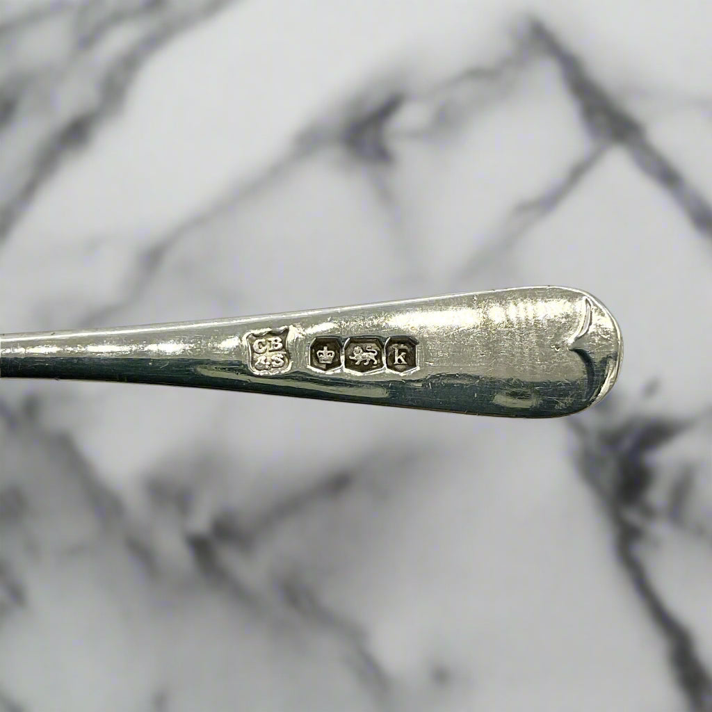 Silver spoon with hallmarks on the handle with a marble background 