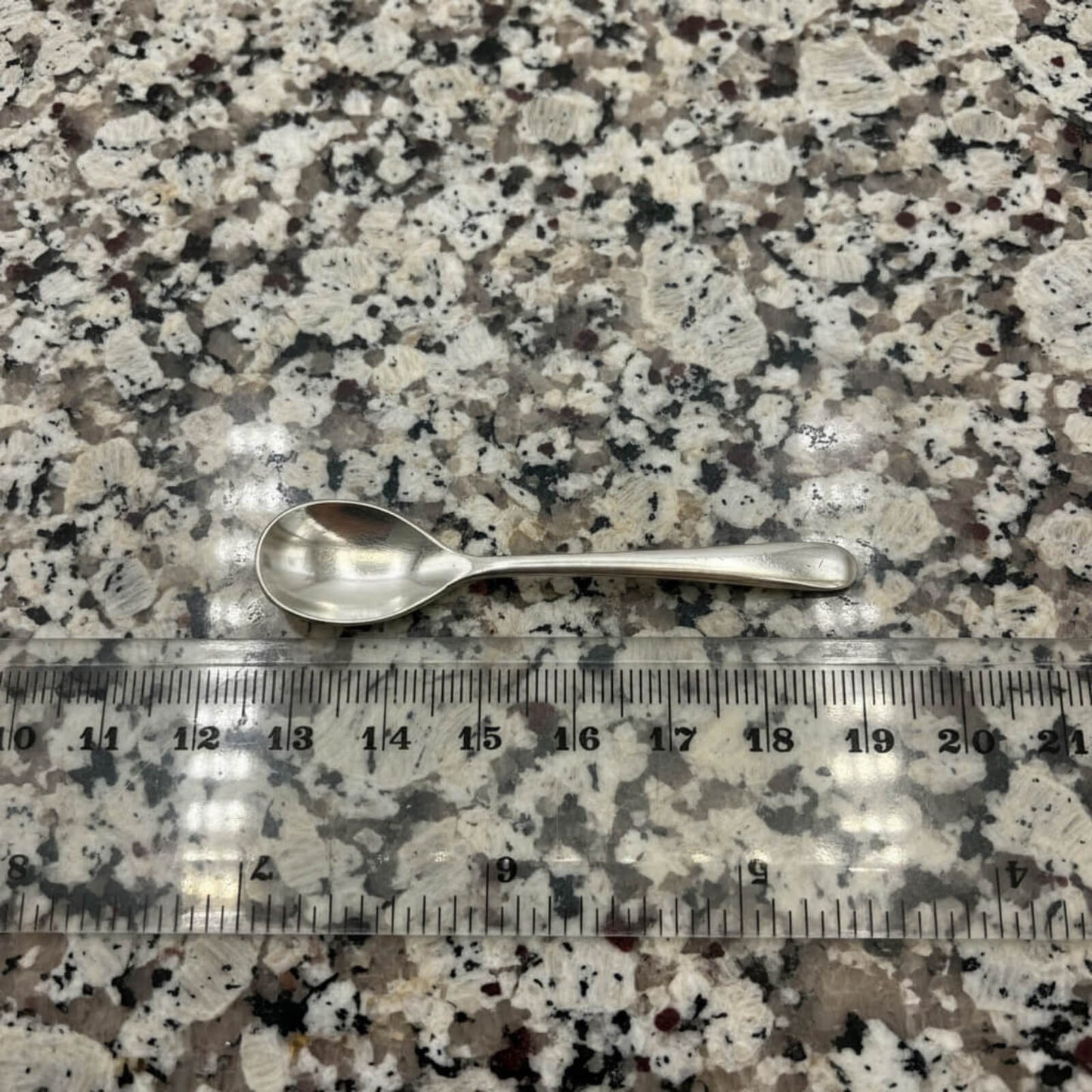 Silver spoon on a speckled granite surface with a ruler for scale.