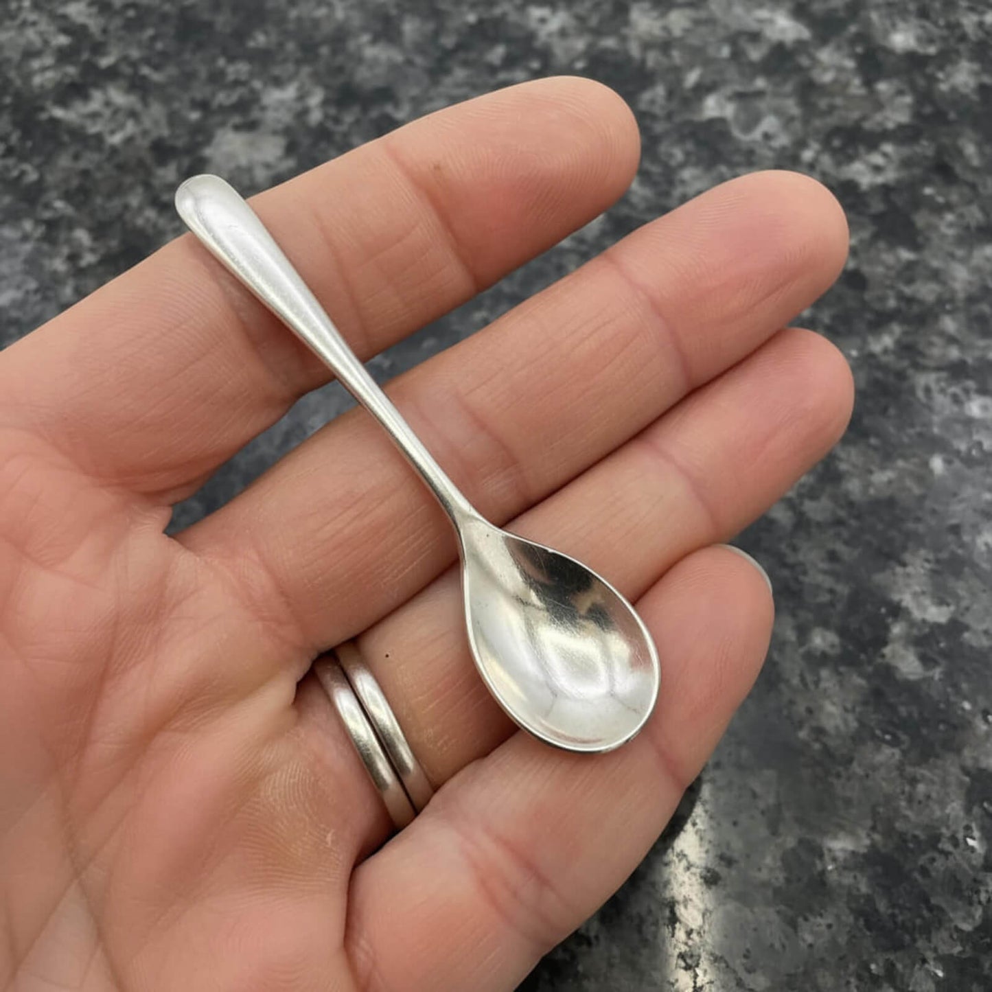 Small silver spoon held in a hand against a dark surface
