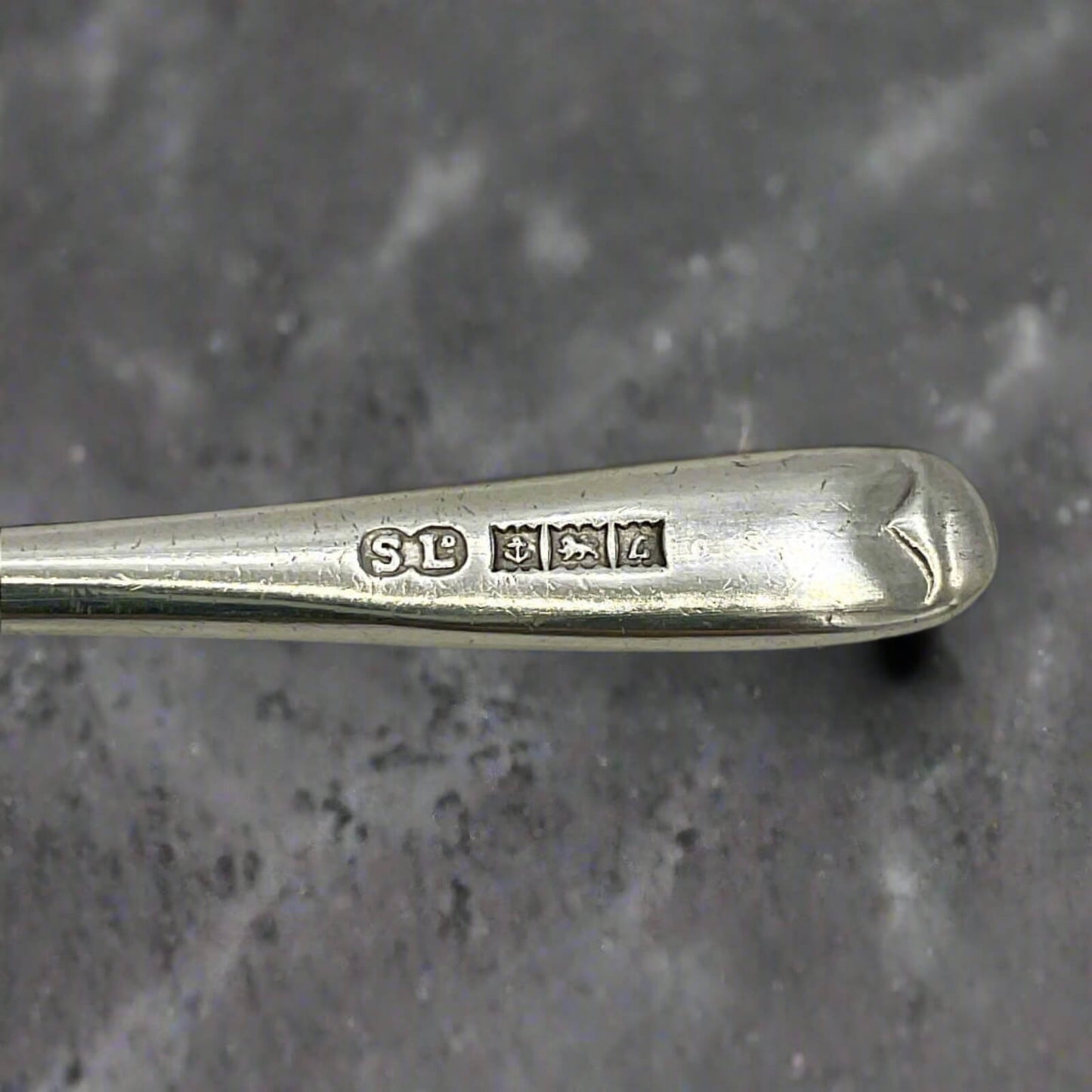 Close-up of a silver spoon handle with engraved marks on a gray background