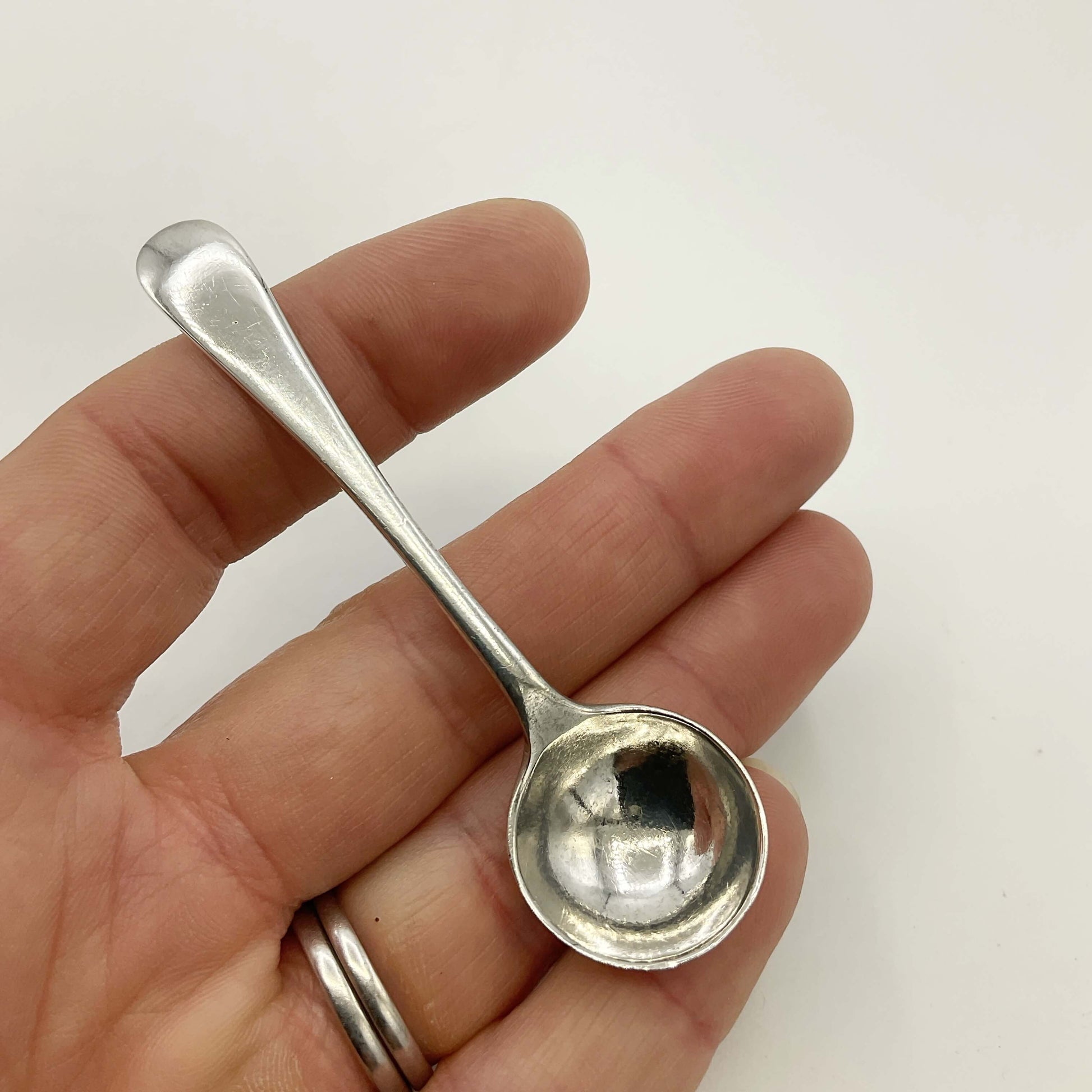 Small silver spoon held in a hand against a white background