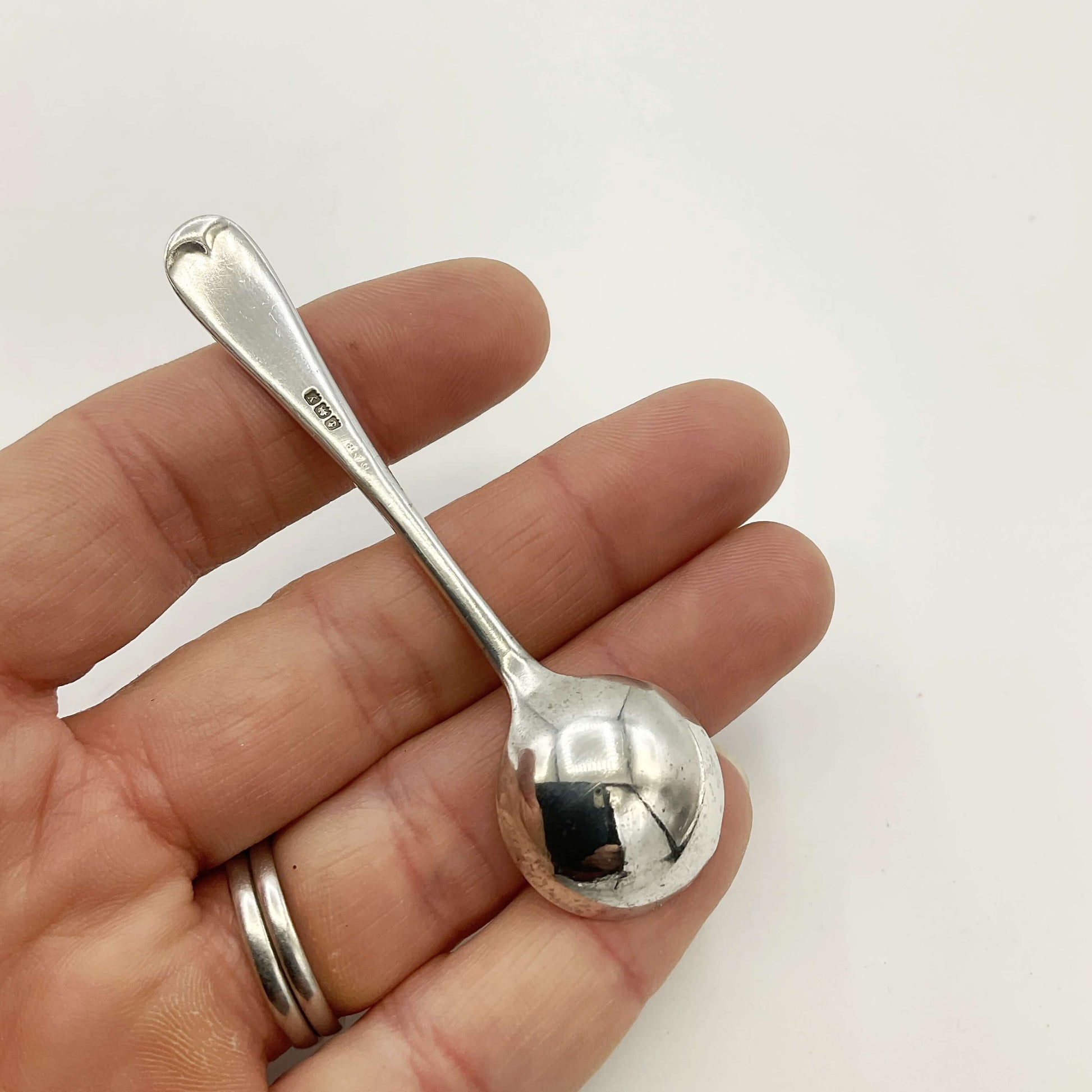 Small silver spoon held in a hand against a white background