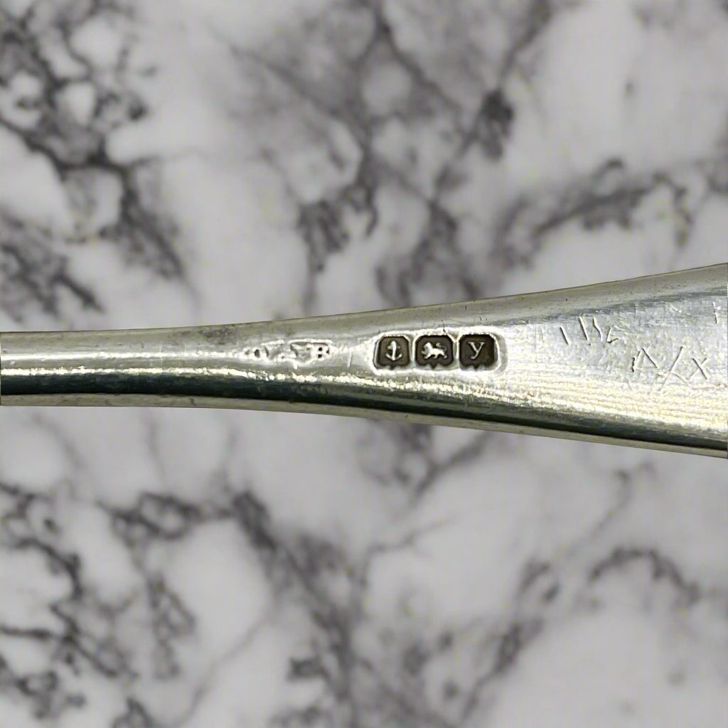 Close-up of a silver spoon handle with hallmarks on a marble background