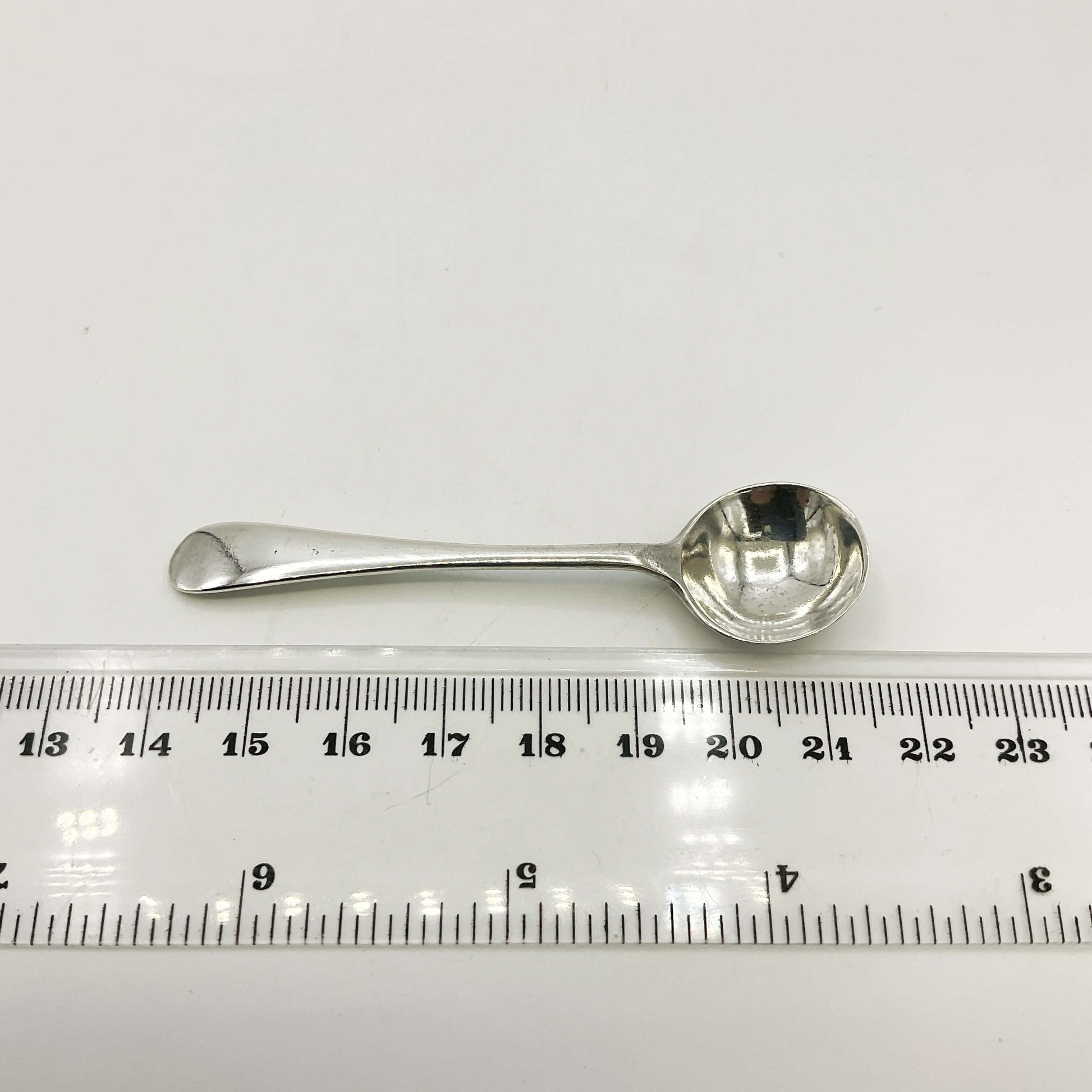 Silver spoon next to a ruler on a white background