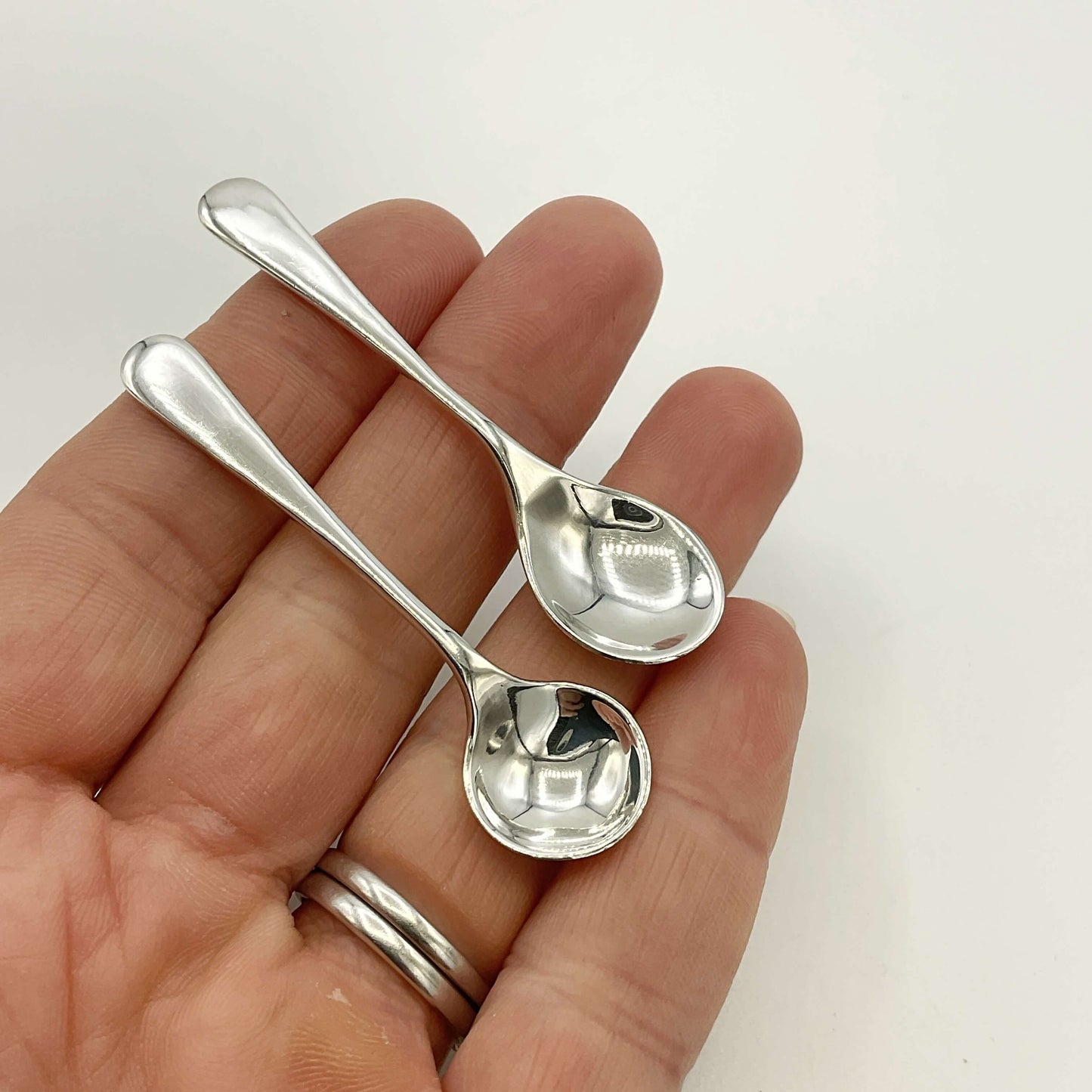 Two small silver spoons held in a hand against a white background