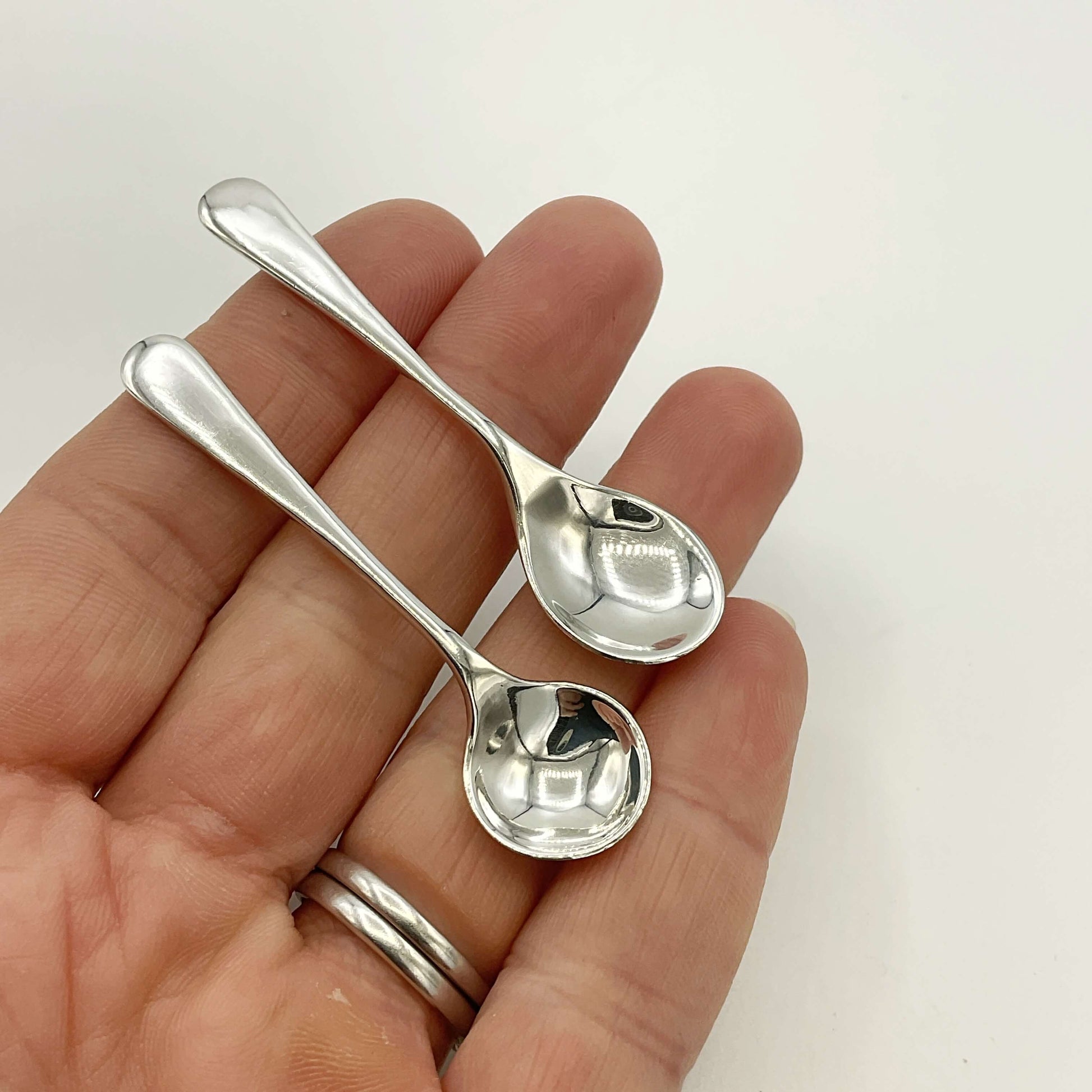 Two small silver spoons held in a hand against a white background