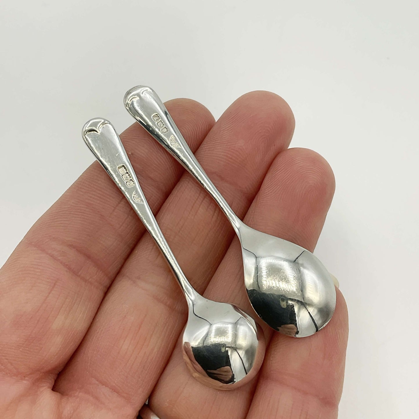 Two silver spoons held in a hand against a white background